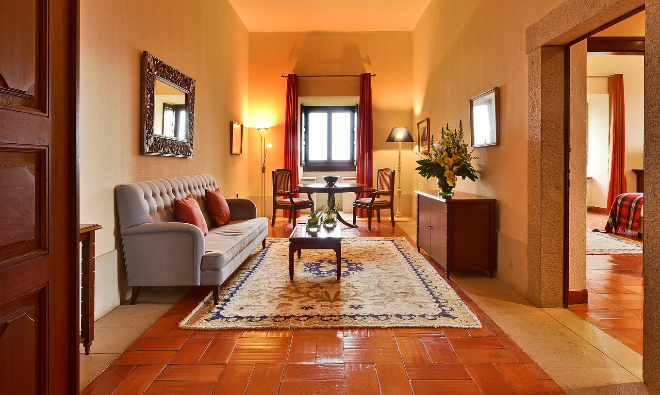 The Special Suite at Pousada Castelo Palmela has a living room with sofa, wooden furniture with a vase of flowers and a table