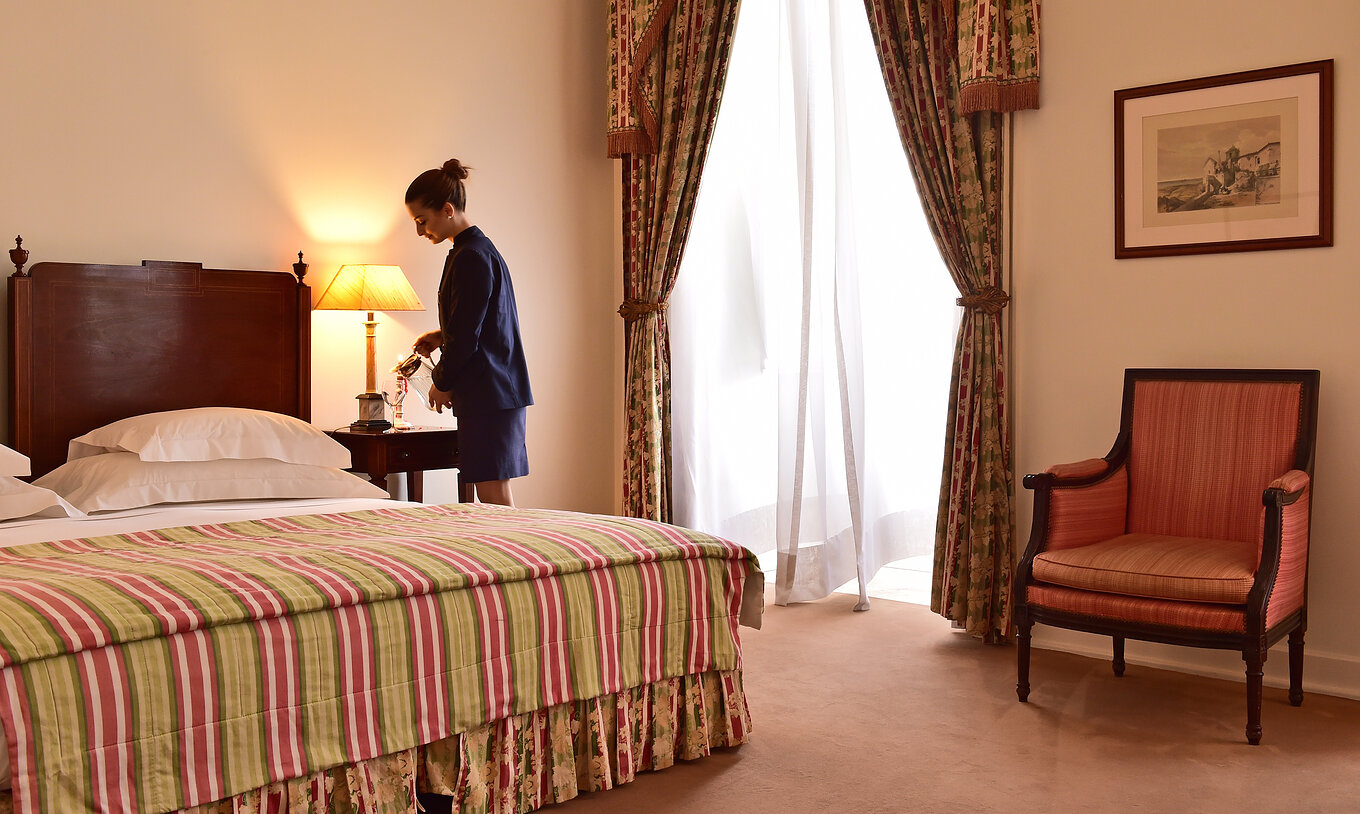 In The Superior Room of The Pousada Palácio Queluz, a woman prepares the room for the upcoming guests