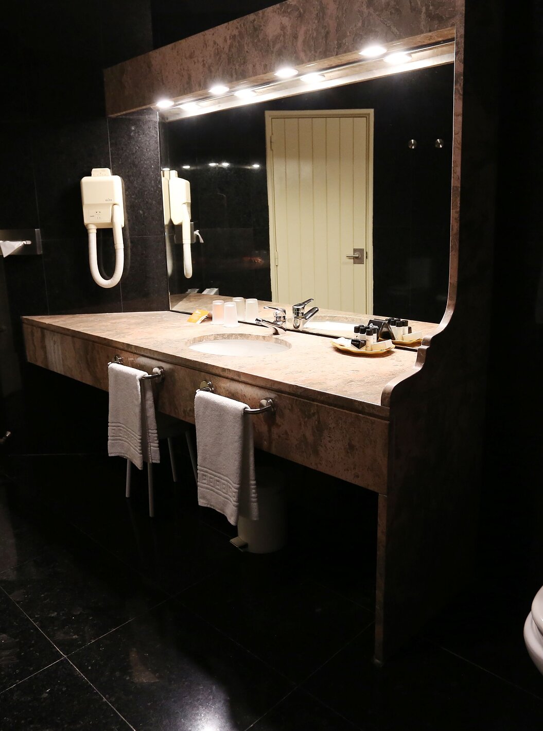 The Classic Room of The Pousada Valença has a dark bathroom with a sink, towels, and a toilet