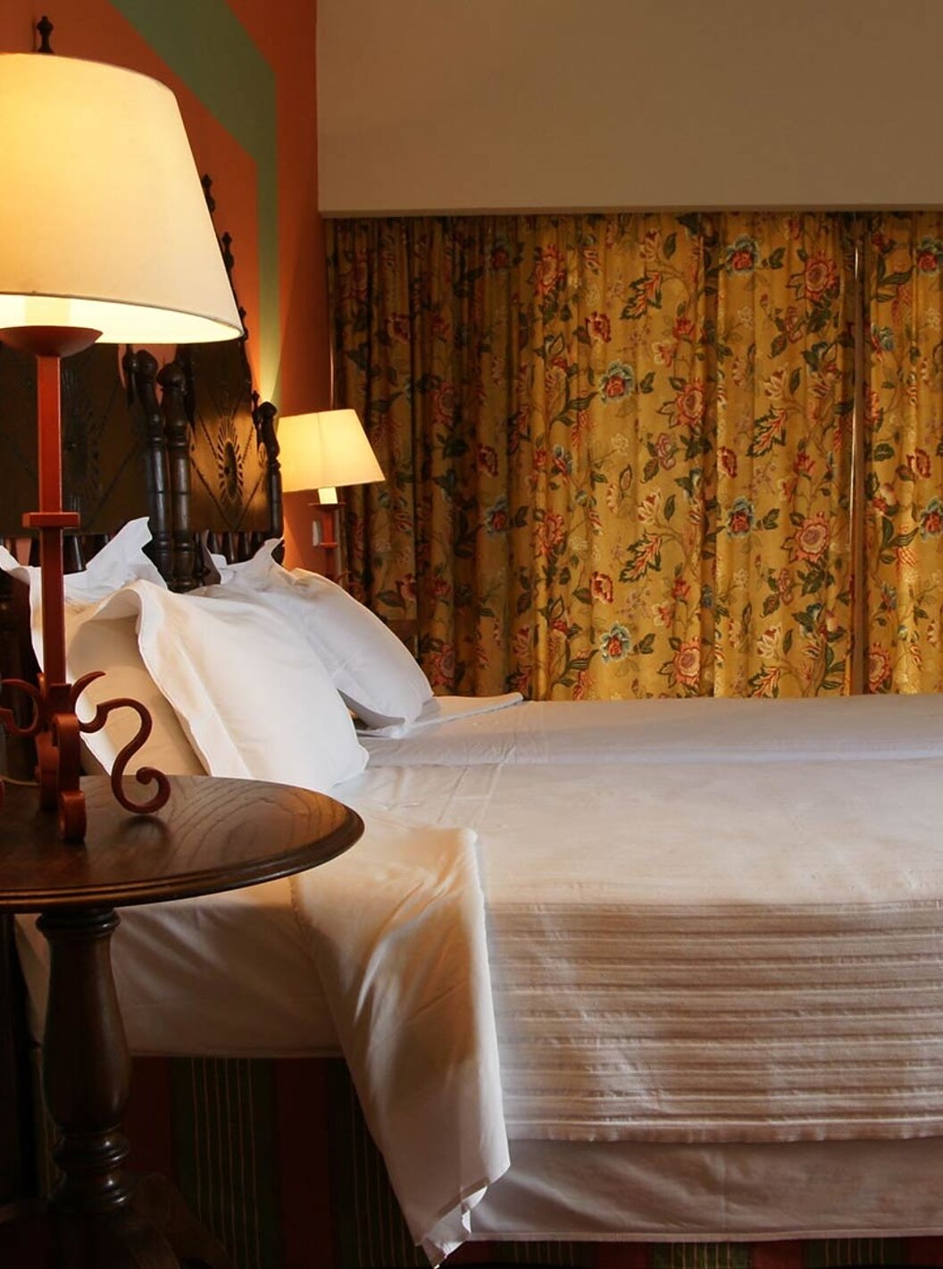 The Junior Suite of The Pousada Valença has two separate beds, a bedside table, an armchair, and a curtain with flowers