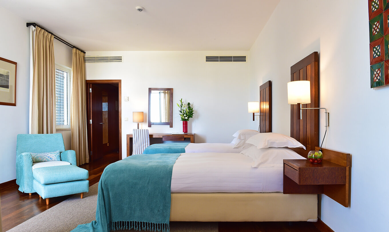The Large Family Room of the Pousada Castelo Alcácer do Sal has two separate beds, with a blue blanket and an armchair