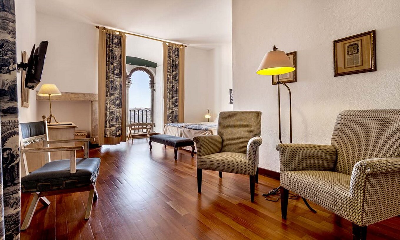 The Large Family Room of the Pousada Castelo Alvito has an entrance hallway with three chairs, a television, and paintings