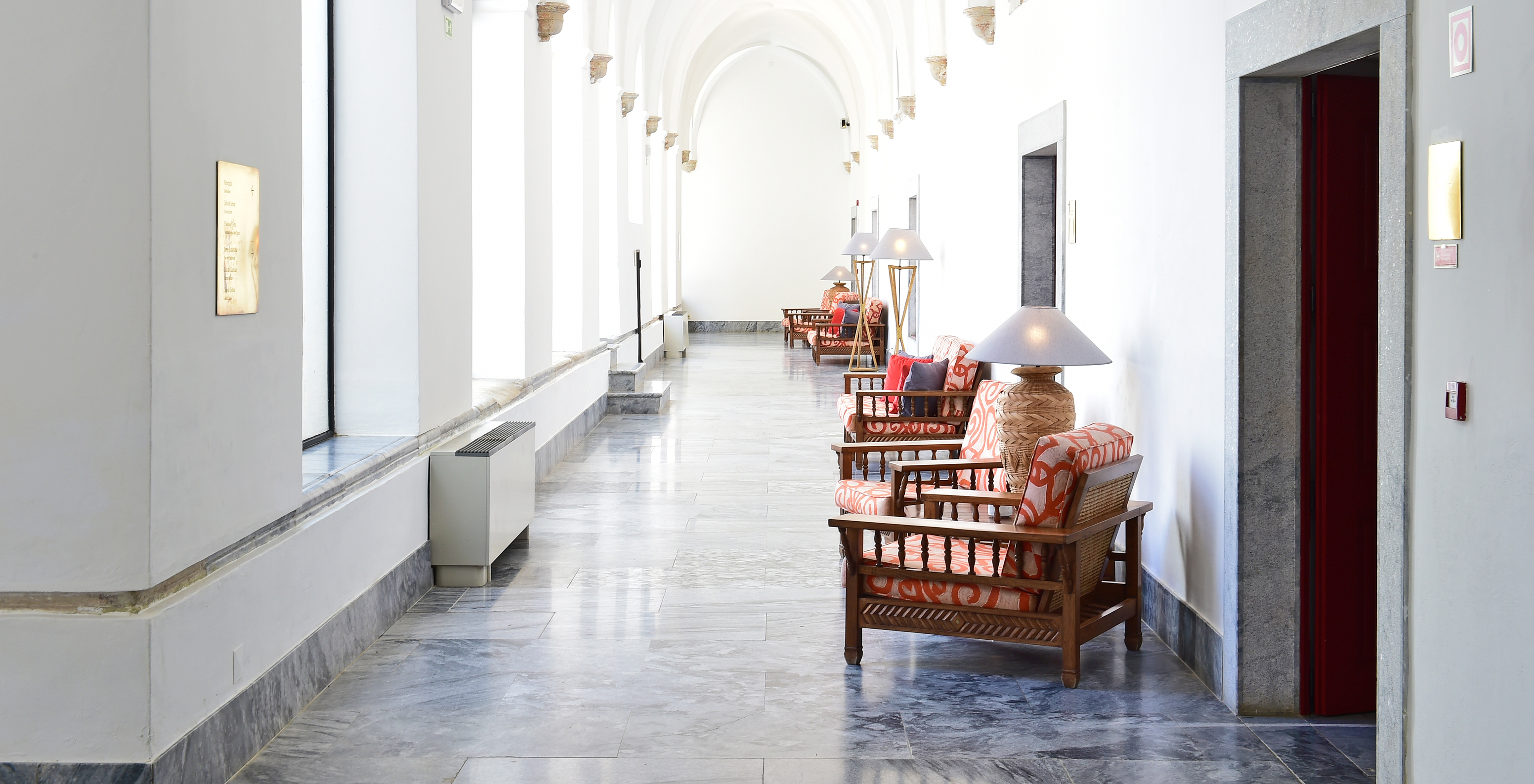 Hallway of Pousada Convento Beja, spacious with a round ceiling and various chairs scattered along the corridor
