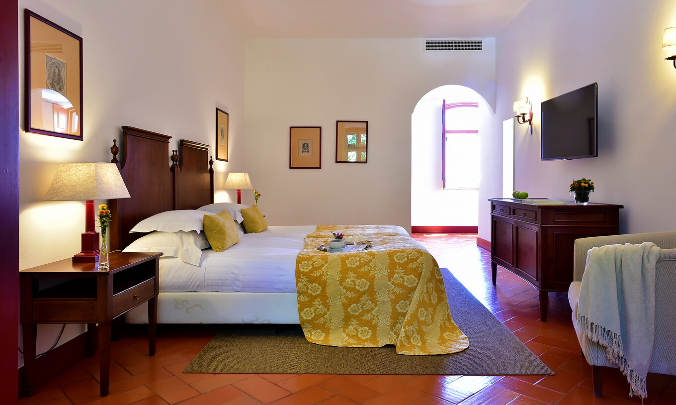 The Family Room of The Pousada Convento Beja has two beds, two bedside tables, and a television