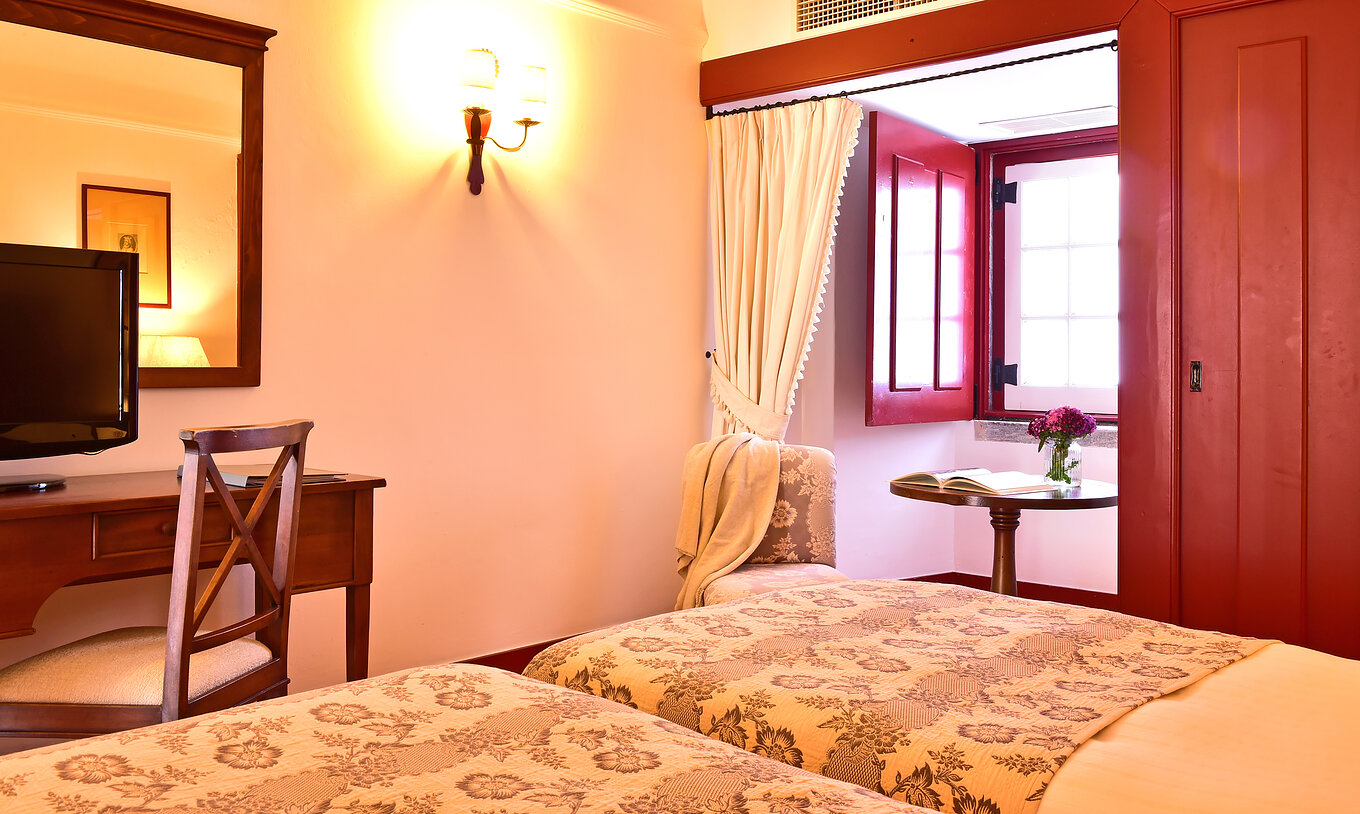 The Superior Room of The Pousada Convento Beja has a side table with a chair by the window of the room