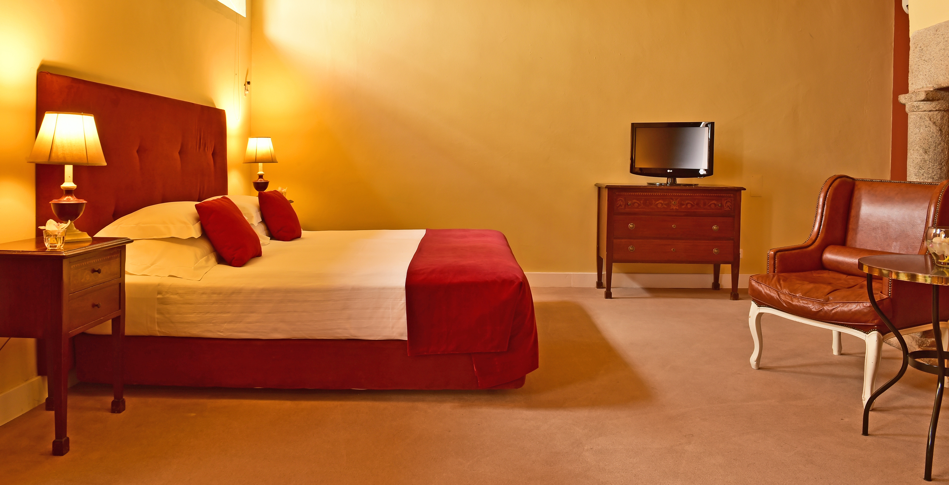The Superior Family of The Pousada Convento Évora has a double bed in red tones, a television, and an armchair