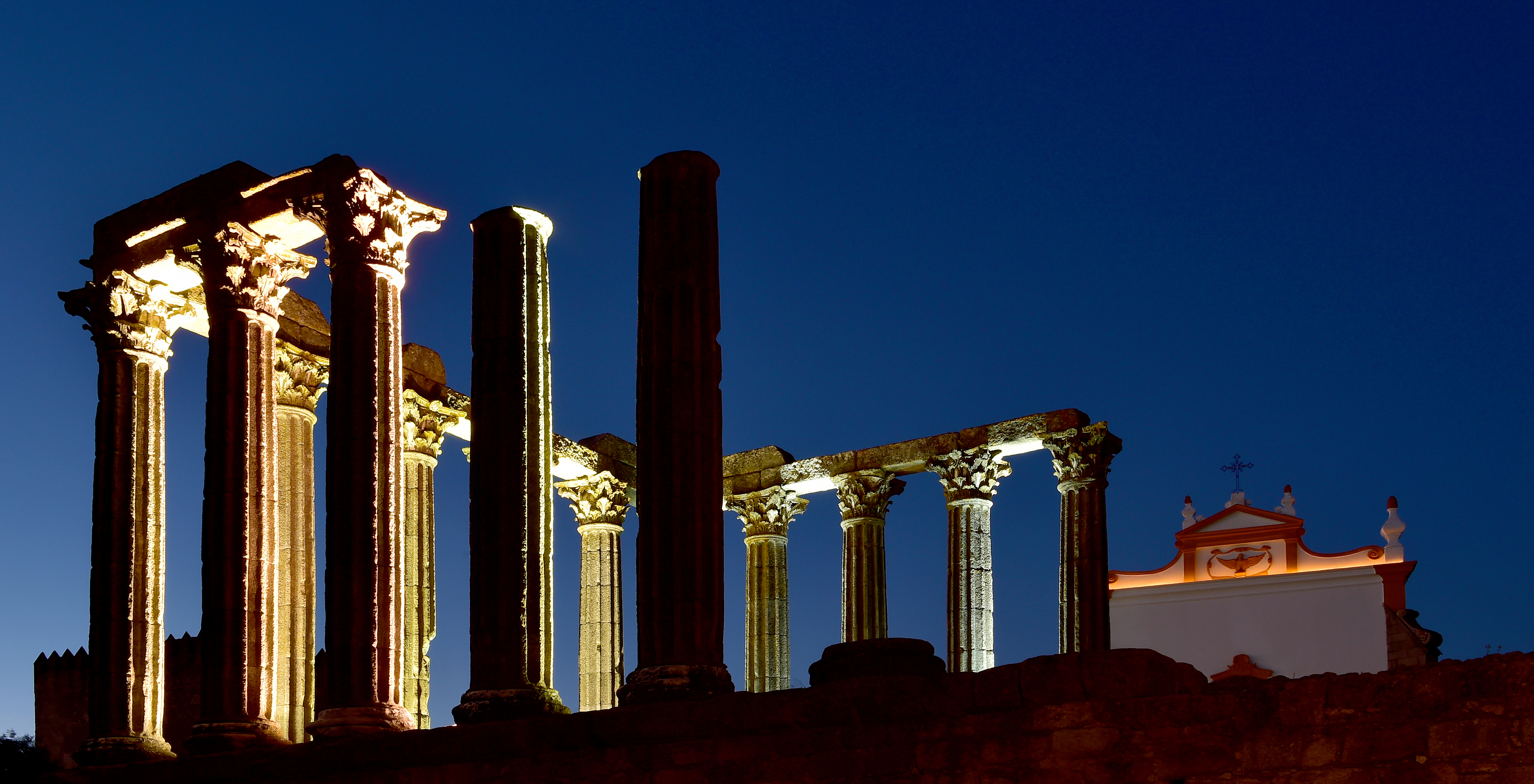 Night view of Diana’s Roman temple in Évora, with illuminated columns and a church in the background