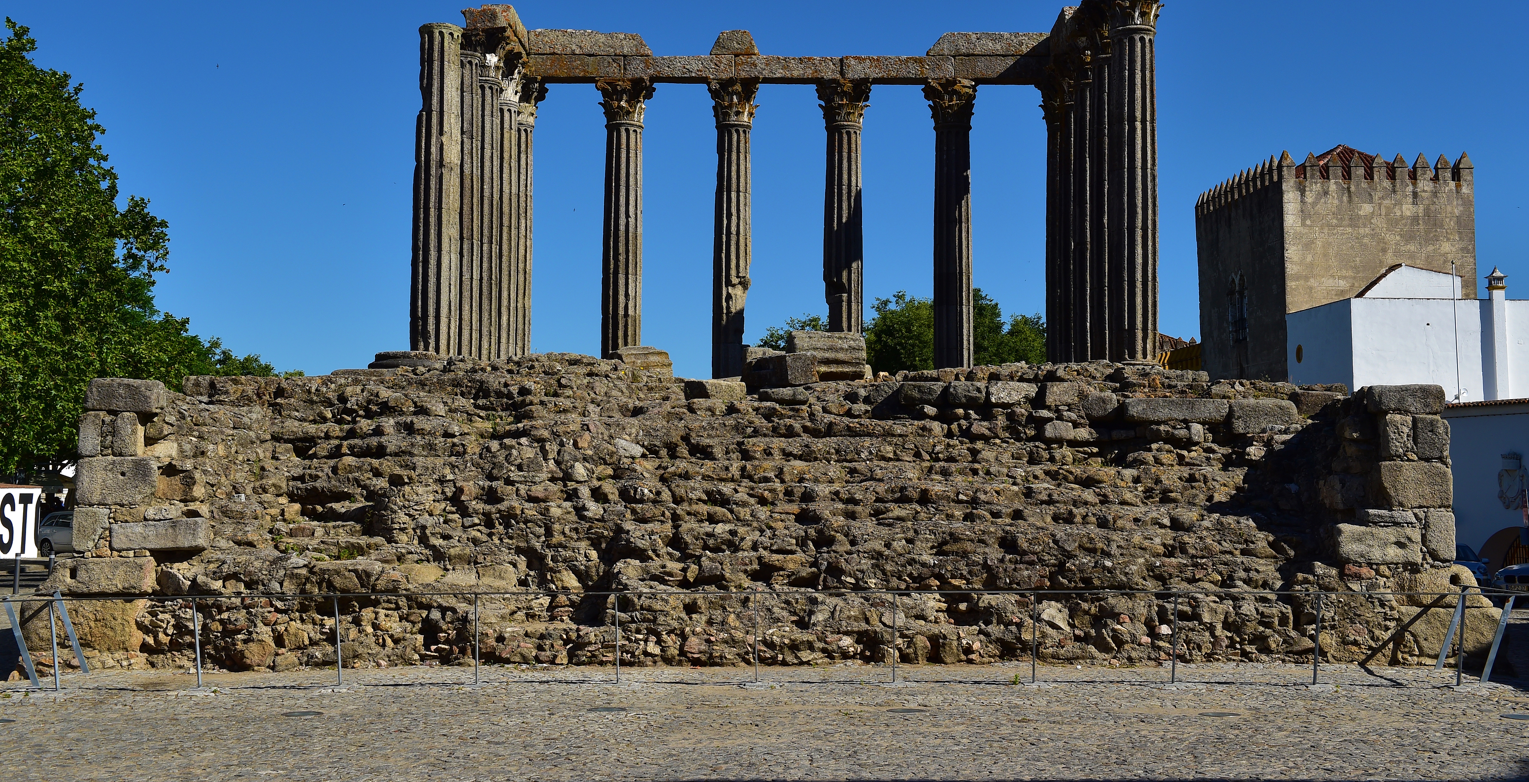 View of the Roman temple of Diana in Évora, with its stone columns and high base, and a tower behind