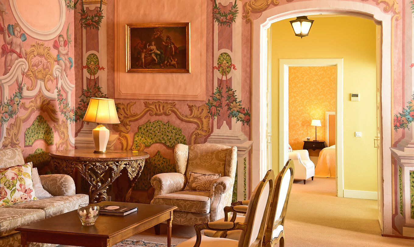 The Master Suite of The Pousada Convento Évora has a living room with a sofa and an armchair and a bed in the background