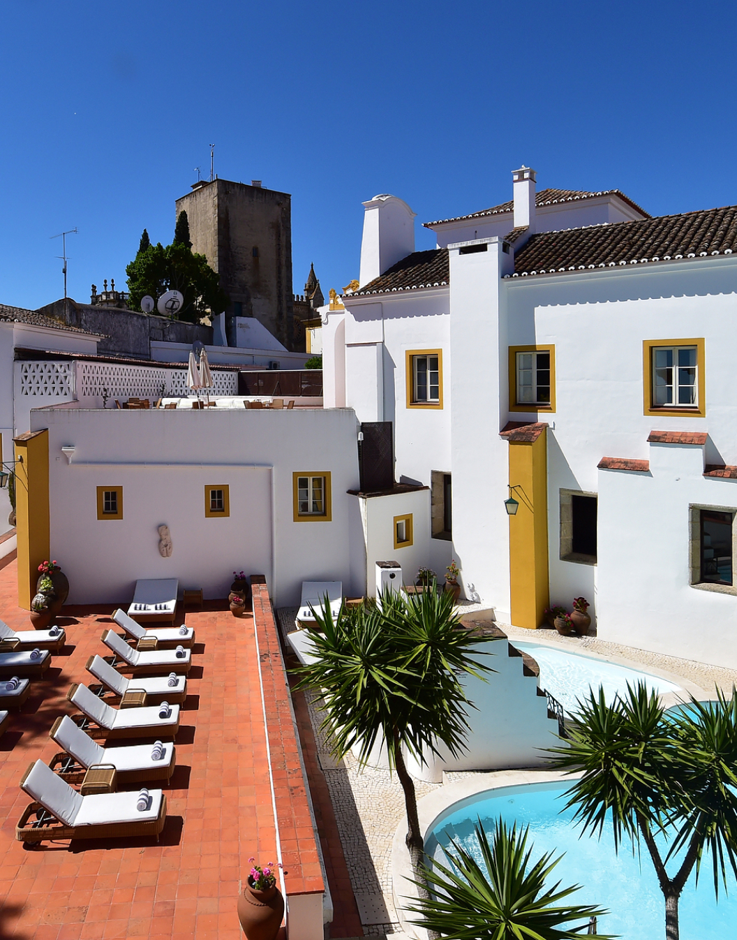 View of the pool, sun loungers, and building of Pousada Convento de Évora, a hotel with a pool in Évora, Alentejo