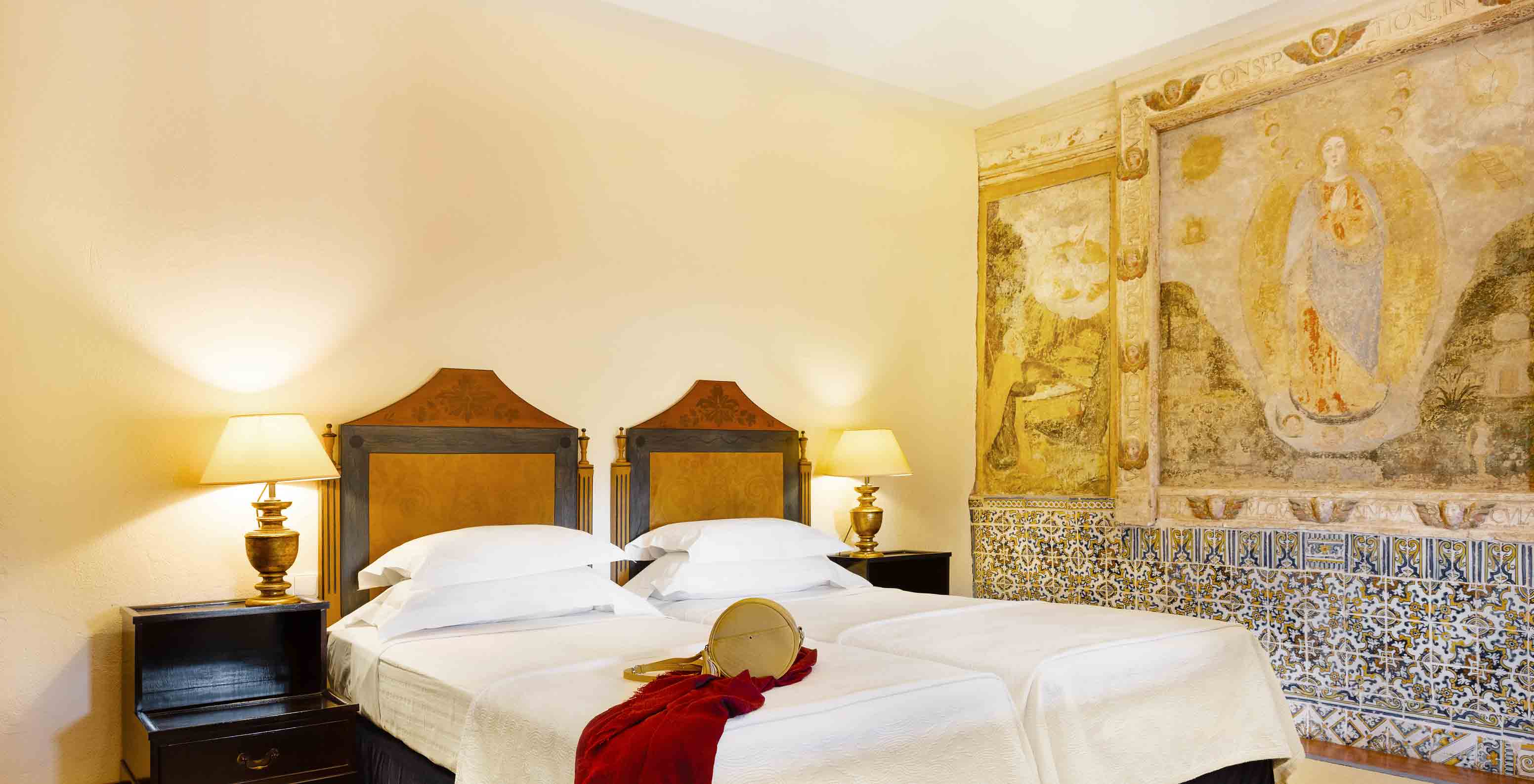 The suite at Pousada Convento Vila Viçosa has twin beds, bedside table with lamp, and tiles on the wall