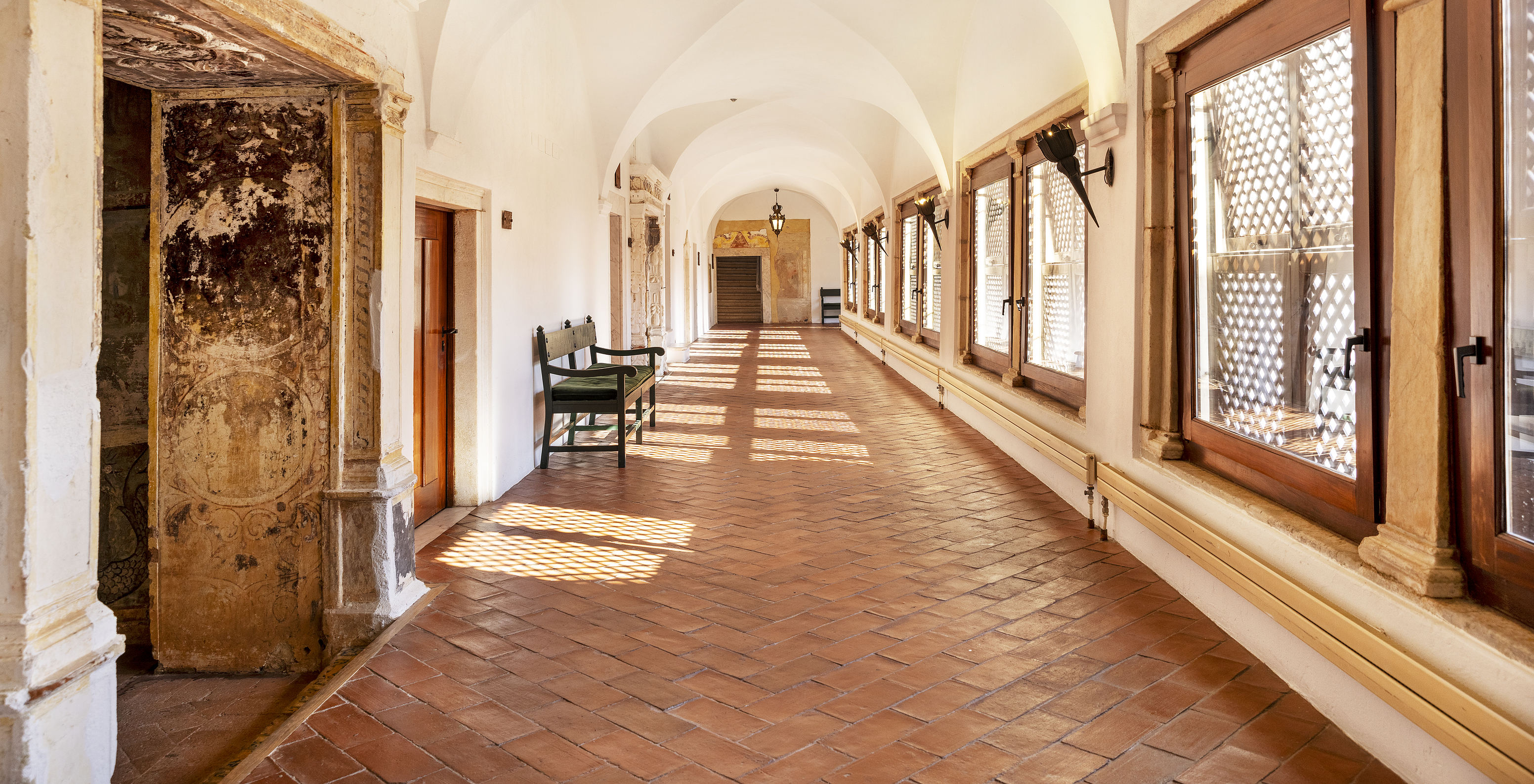 Hallway in a historic building in a hotel in Vila Viçosa, with several windows along the corridor and a green bench