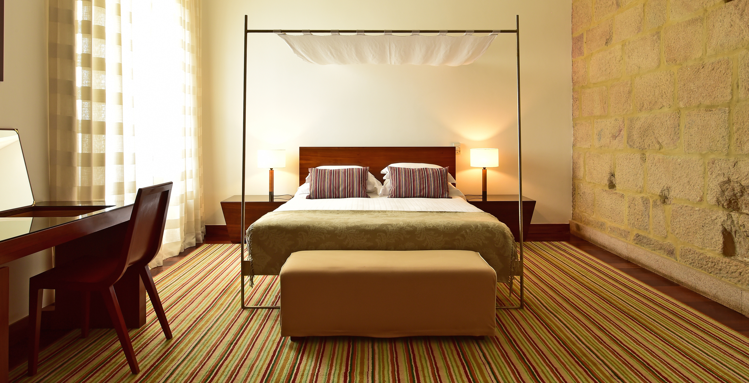 The Historical Superior Room of The Pousada Mosteiro Crato has stone walls with a four-poster double bed and a stool