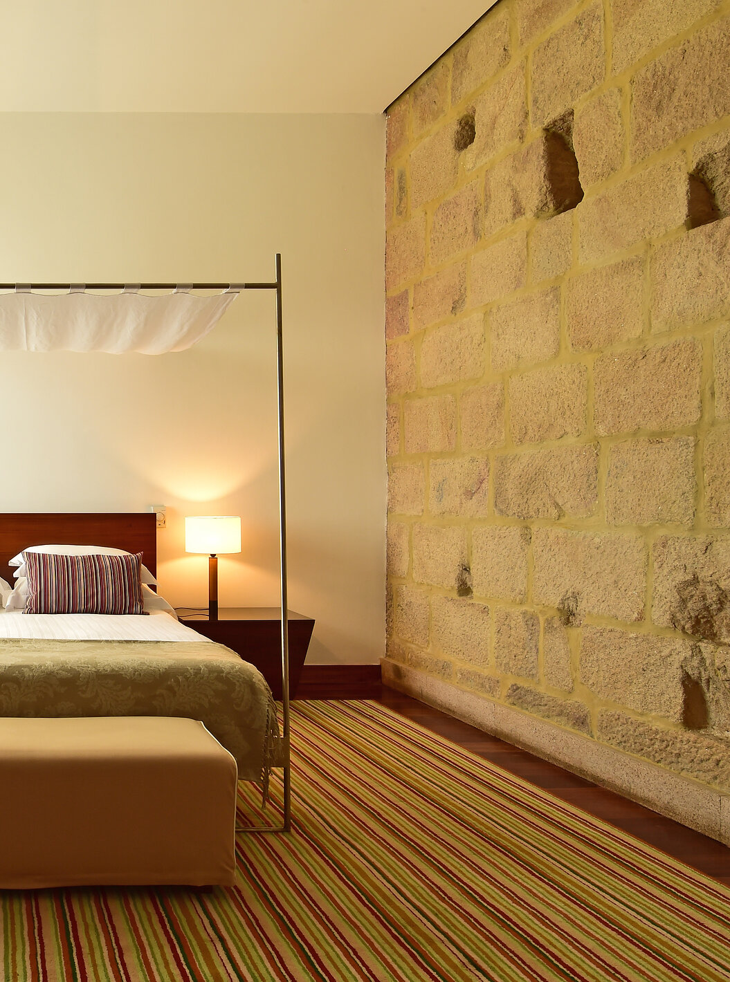 The Historical Superior Room of The Pousada Mosteiro Crato has stone walls with a four-poster double bed and a stool