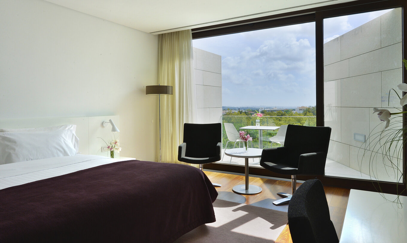 The Superior Room of The Pousada Palácio Estoi features a bed, a table with two chairs, and a window with balcony access