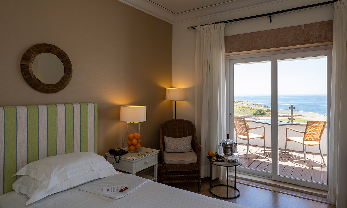 The Superior Room of Pousada Sagres has a balcony with table and chairs, a bed with striped headboard, and snacks
