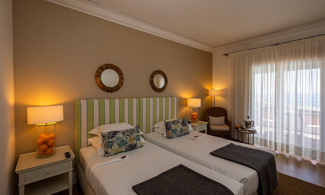 The Superior Room of Pousada Sagres has two beds with striped headboards, two round mirrors, and a balcony