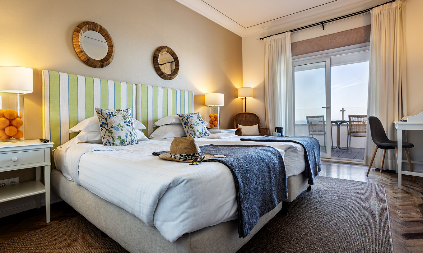 The Superior Sea View Room of Pousada Sagres has two beds with striped headboards, two round mirrors, and a balcony