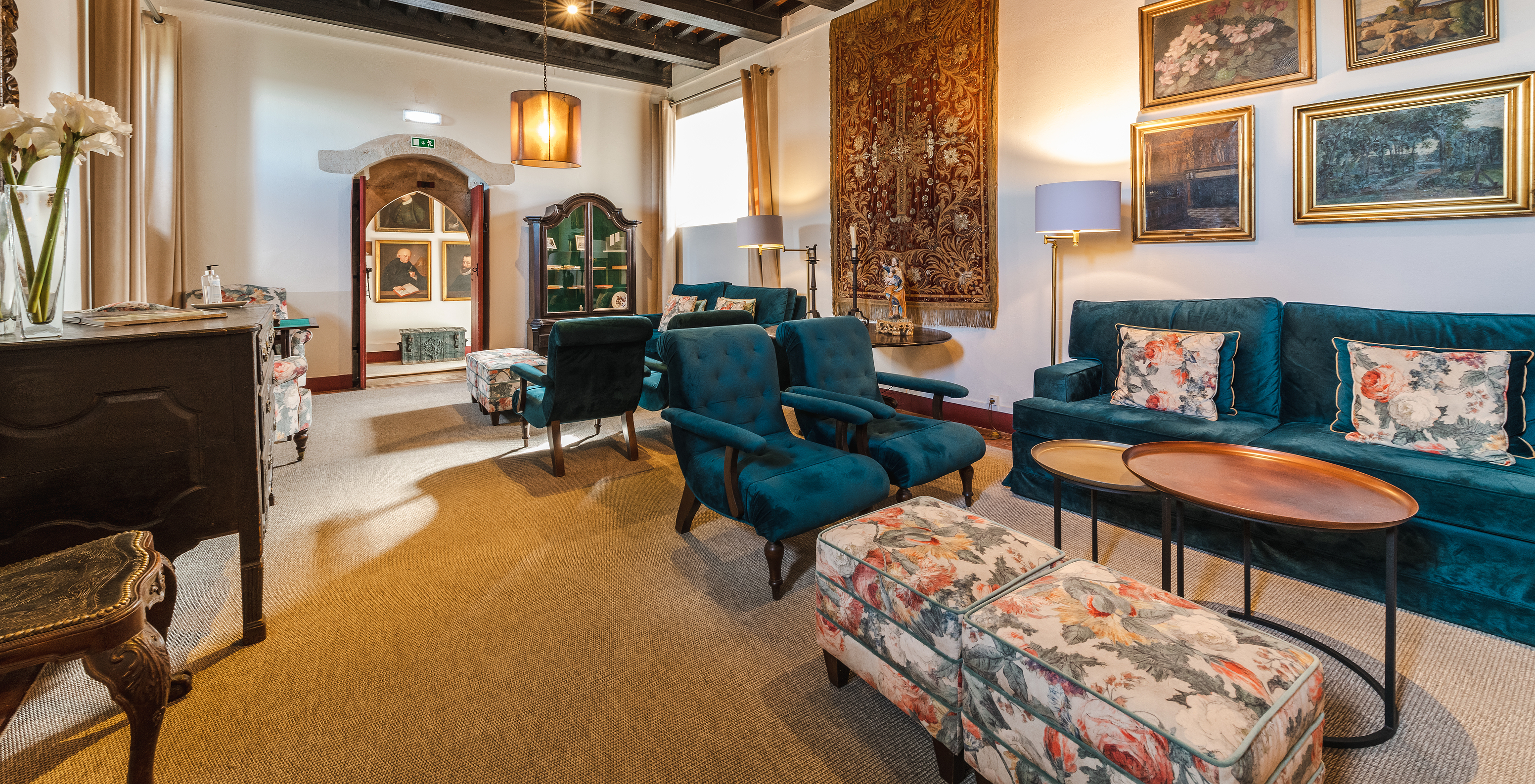 Space in Pousada Castelo Óbidos with various blue sofas and armchairs, with medieval paintings and rugs on the walls