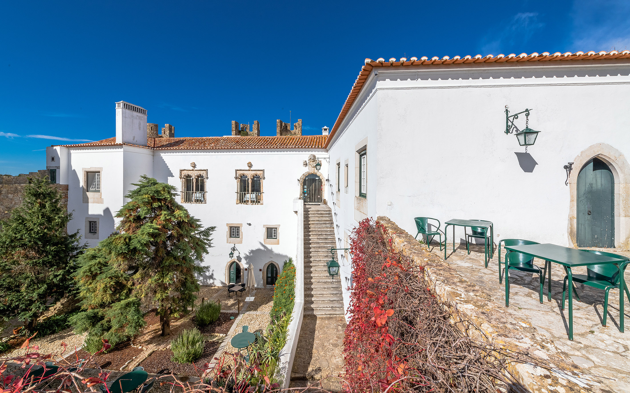 Exterior view of the façade of Pousada Castelo Óbidos, with its gardens, chairs, and tables around