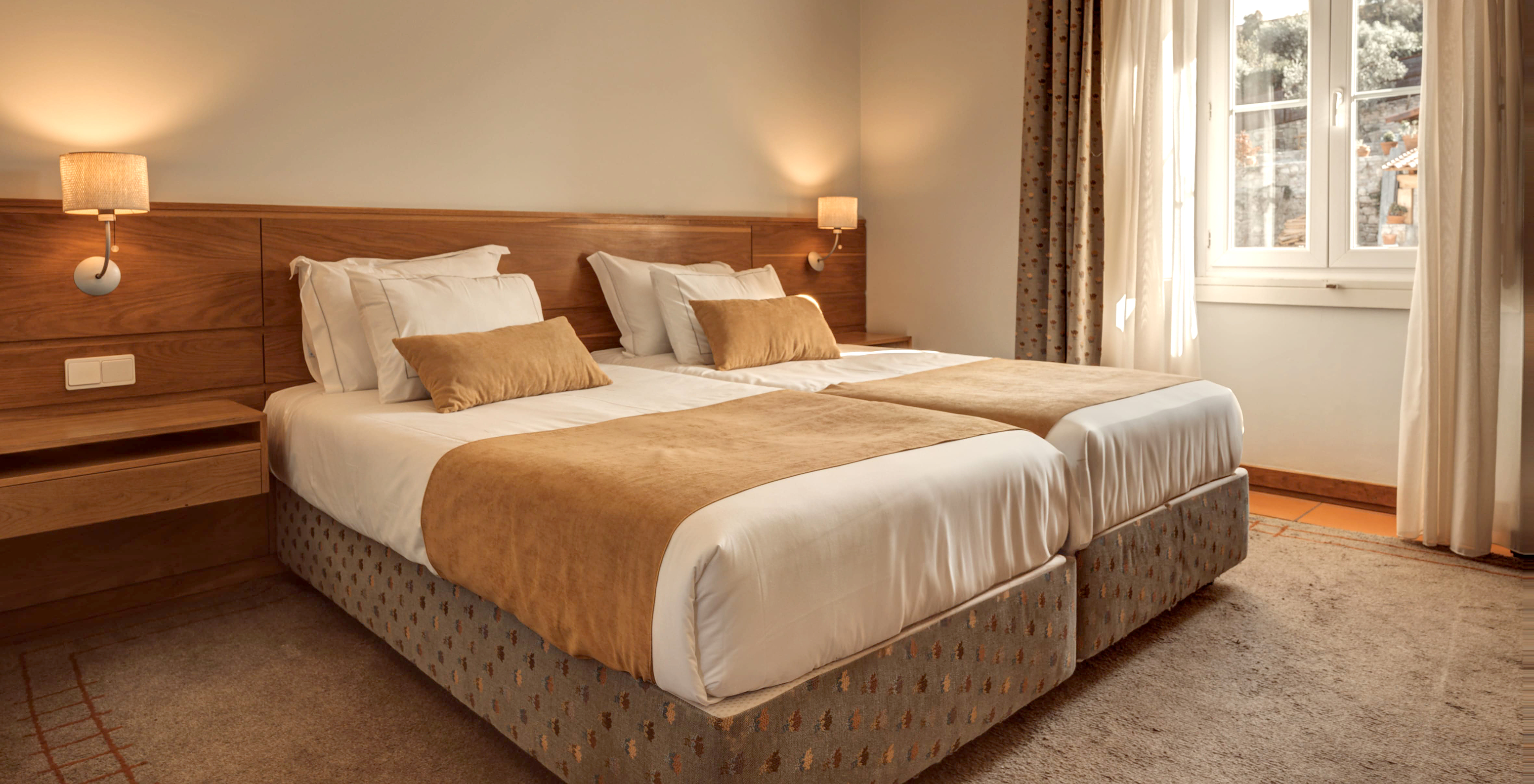 The Superior Room of The Pousada Ourém has two joined beds with a window beside it overlooking other houses