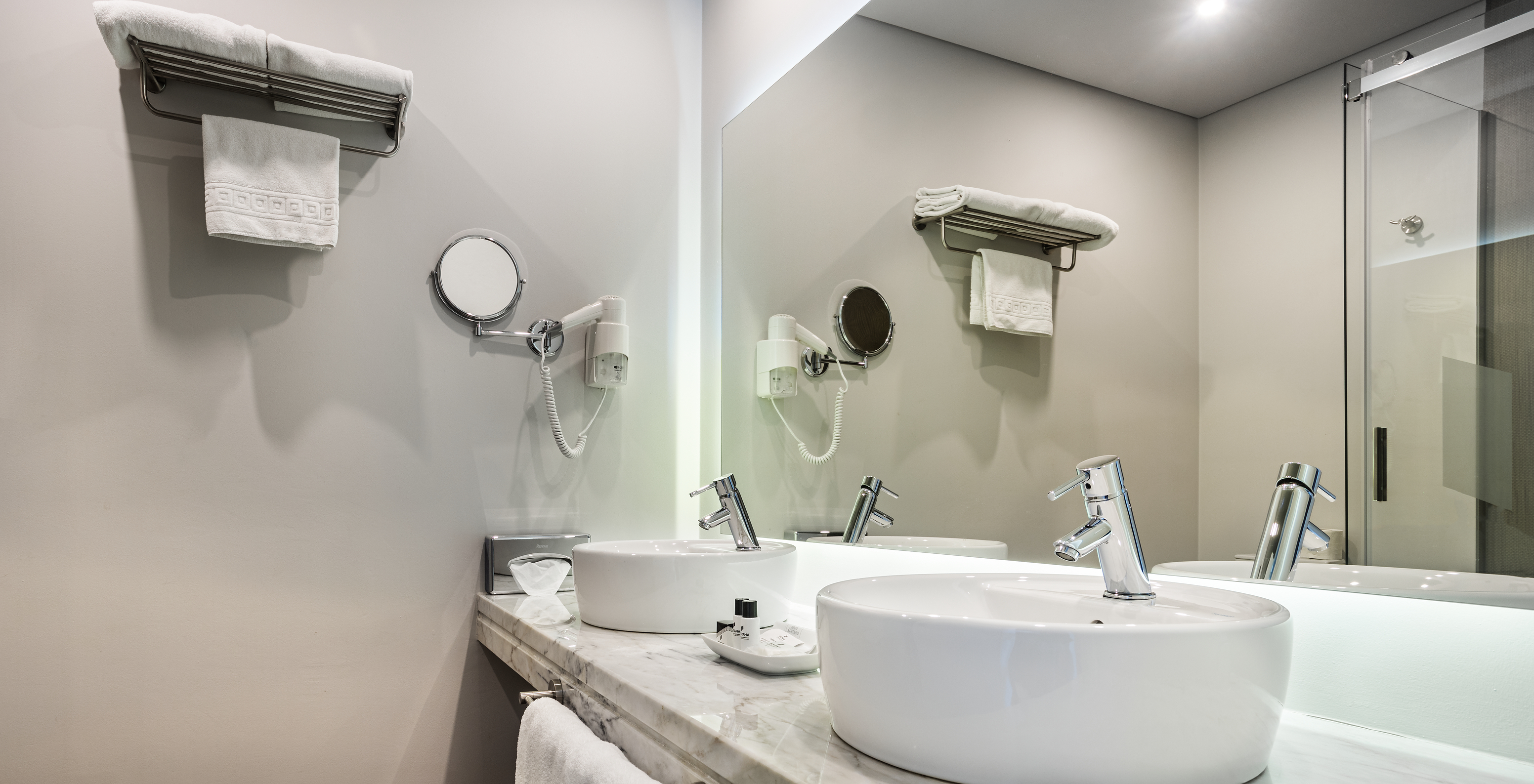 The Superior Large Family Room of The Ria Inn - Aveiro has two sinks, a large mirror, towels, and a hairdryer