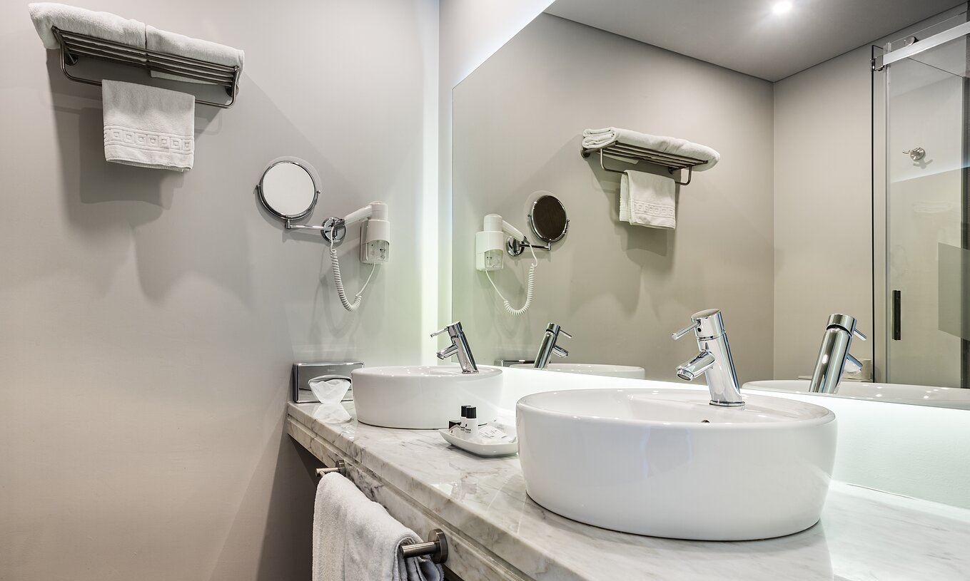 The Superior Large Family Room of The Ria Inn - Aveiro has two sinks, a large mirror, towels, and a hairdryer