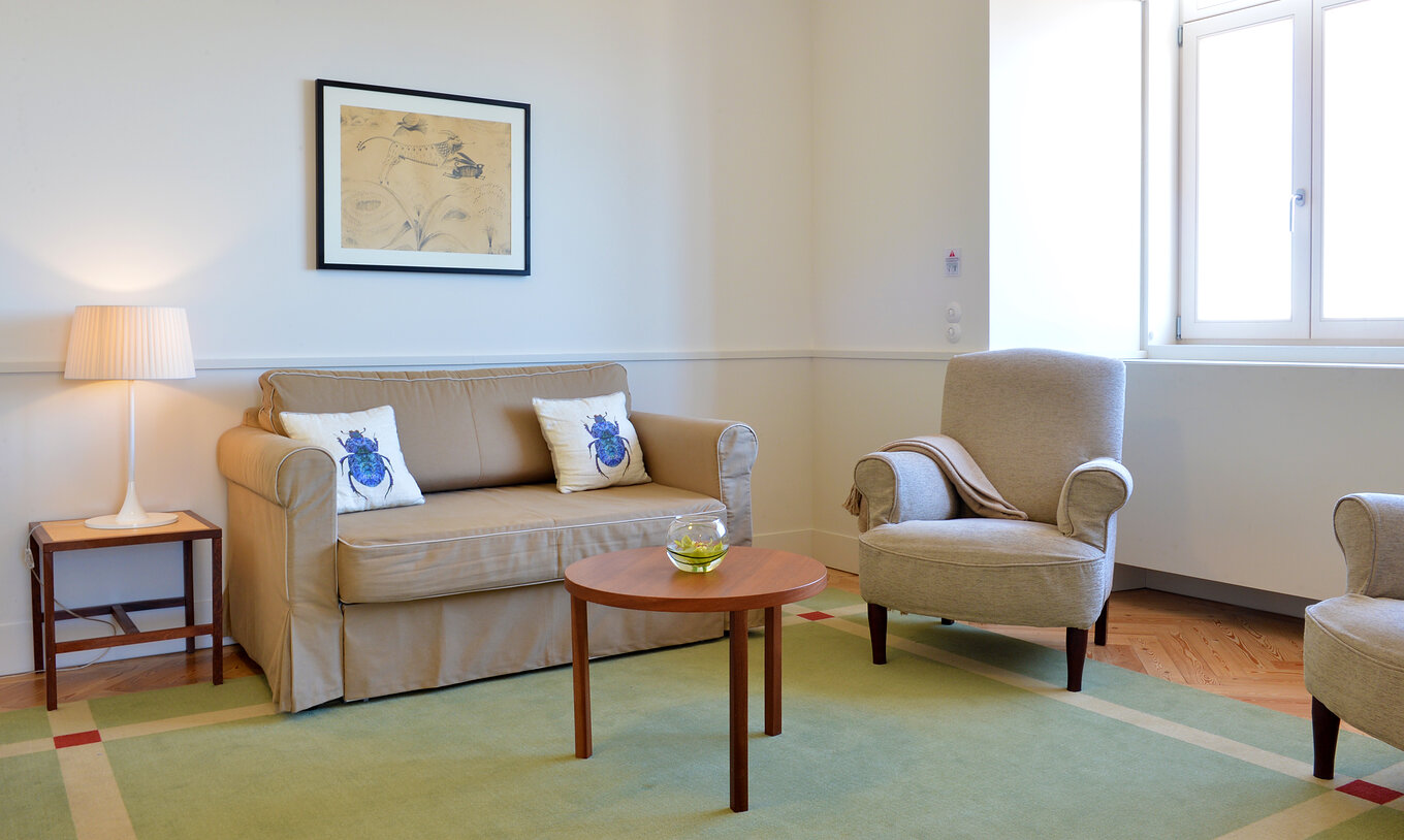The Large Family Room of The Serra da Estrela Inn has a living room with a painting, sofa, table, two armchairs and a window