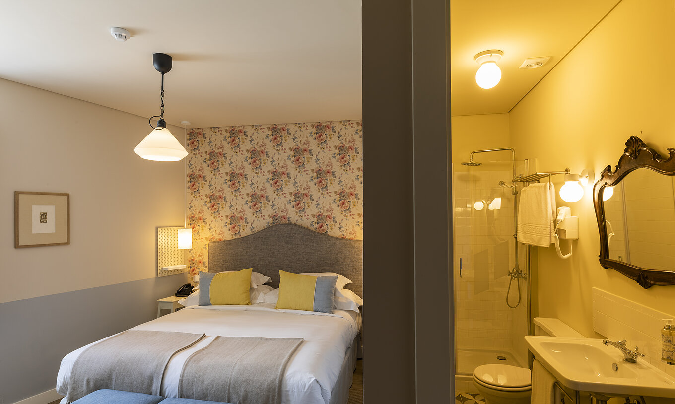 The Classic Room of The Pousada Vila Óbidos has a double bed, floral wallpaper, and a bathroom with a shower and toilet