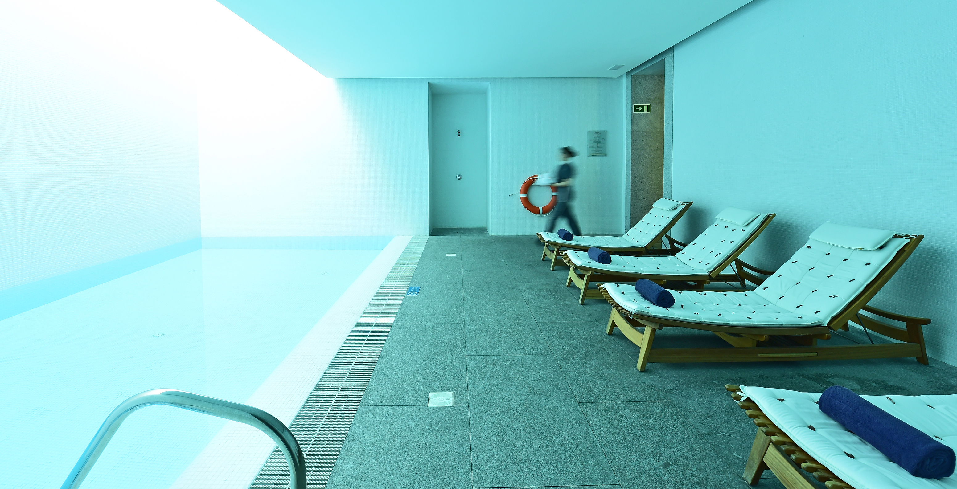 Heated indoor pool with cushioned sun loungers and towels