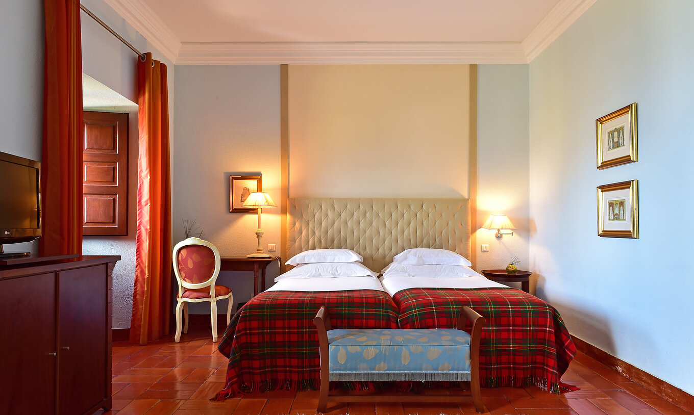 The Classic Family Room at Pousada Castelo Palmela has two beds, a bedside table, a wooden desk, and a window