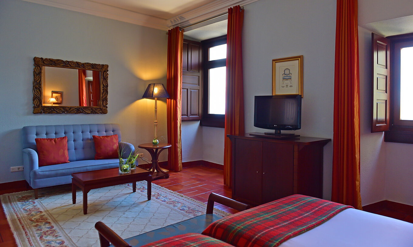 The Classic Room at Pousada Castelo Palmela has a blue sofa, a coffee table with two vases, television, and two windows