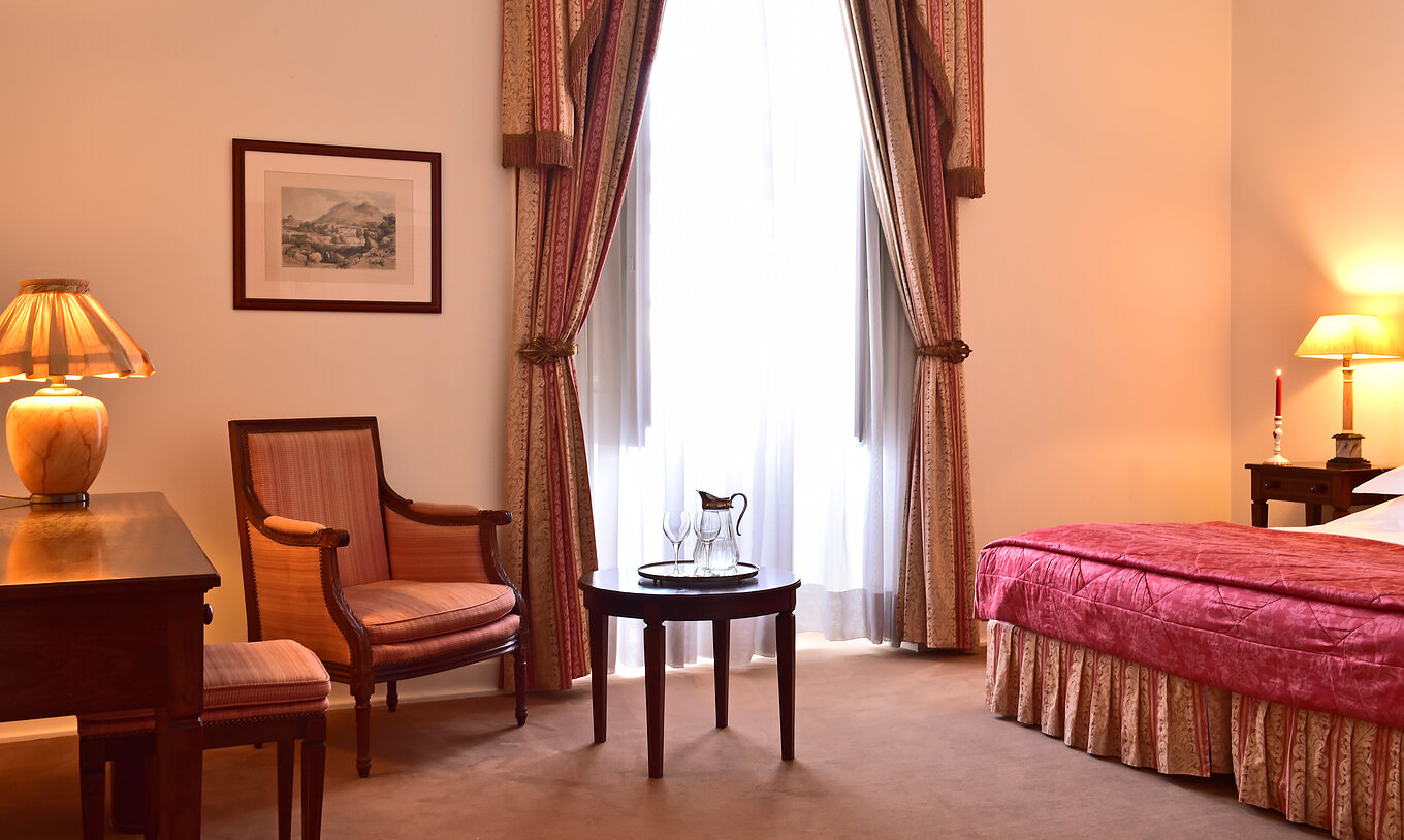 The Standard Suite of The Pousada Palácio Queluz features an armchair and a table near the bed and window where you can rest