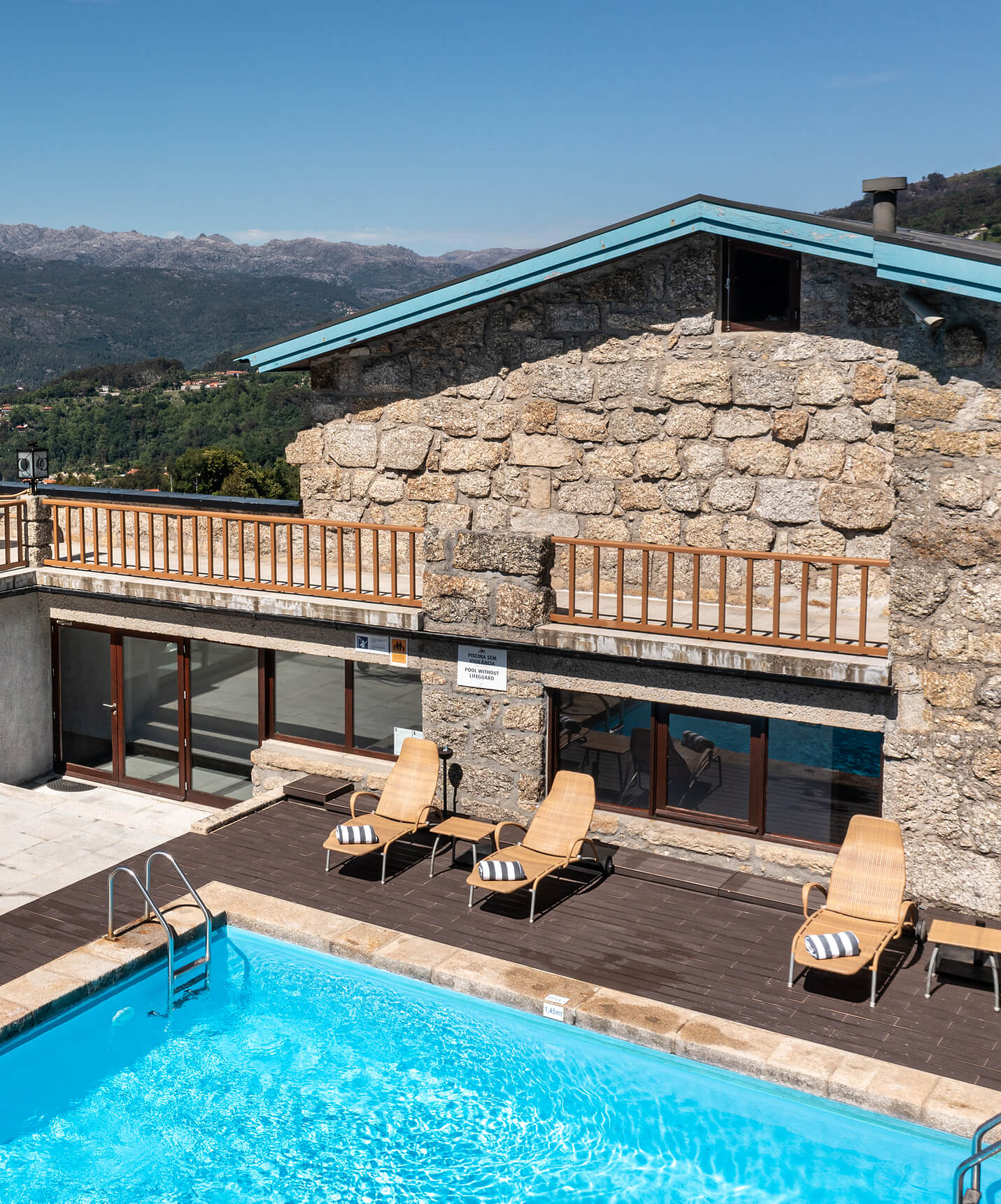 Outdoor pool at the Hotel in Peneda-Gerês National Park, with sandy-colored sun loungers and the building in the background