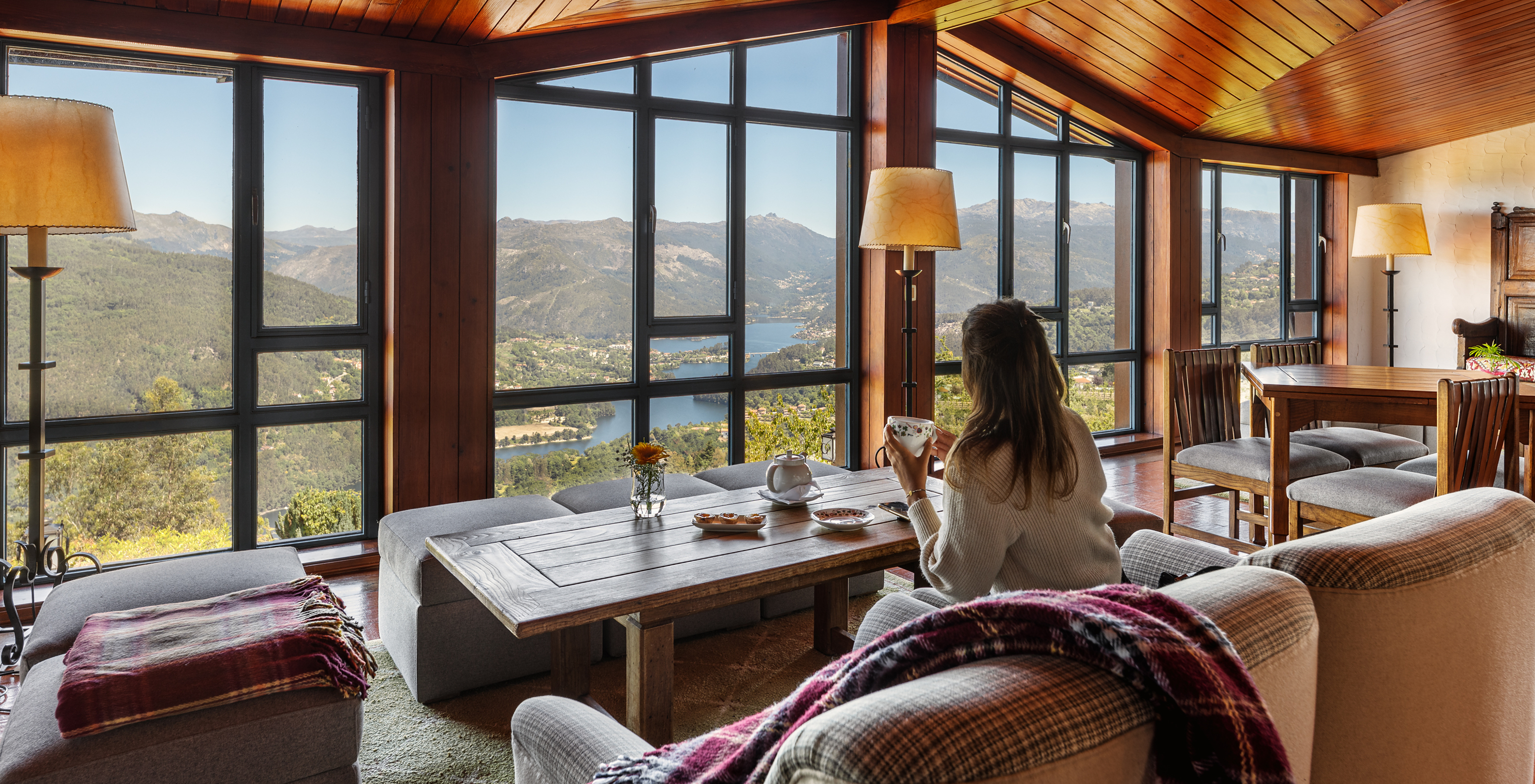 Seating area, with sofas, blankets and tables, with a large window overlooking the Douro River and mountains