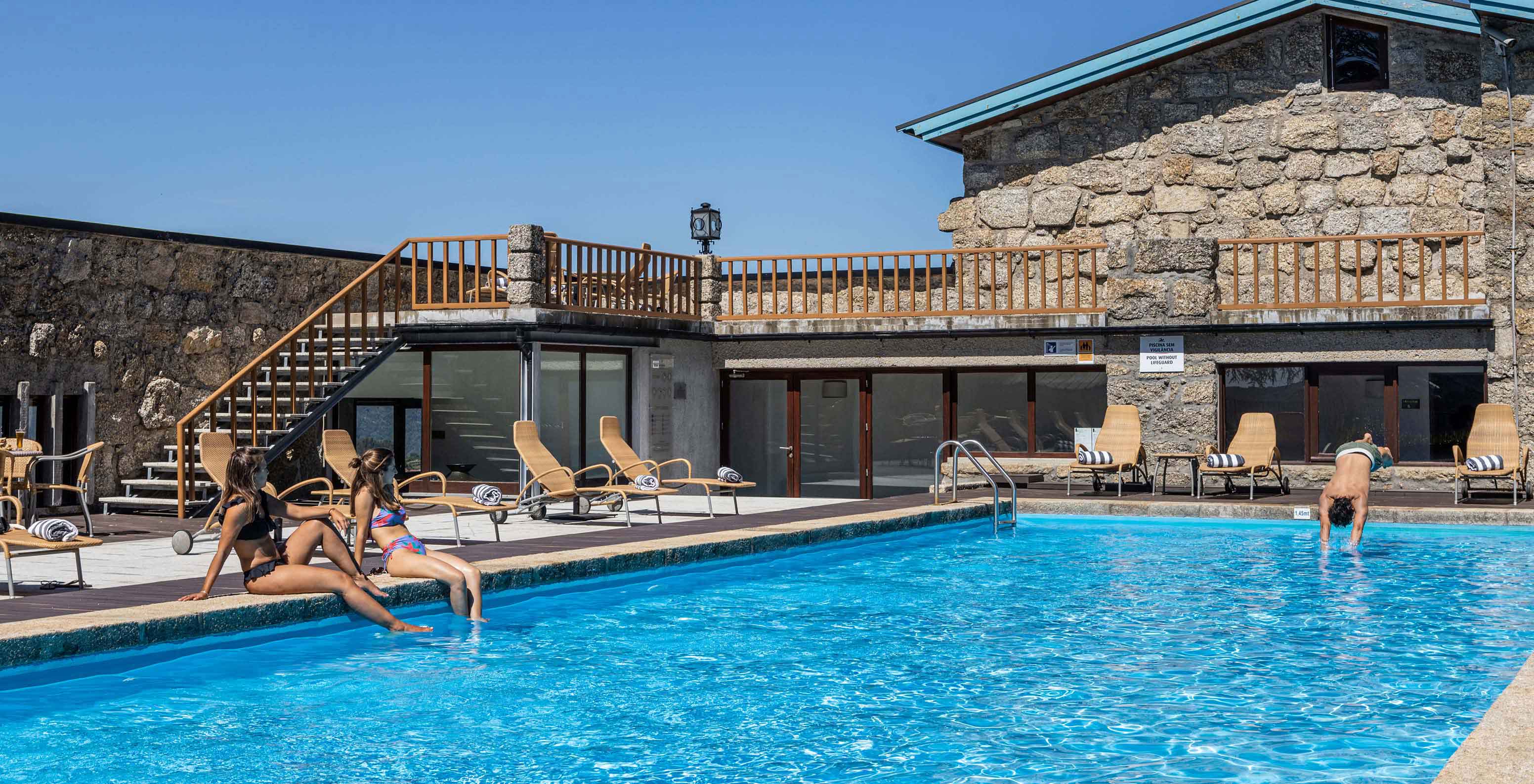 Guests relax sitting on the edge of the outdoor pool at Pousada Caniçada - Gerês, Mountain Hotel in Gerês