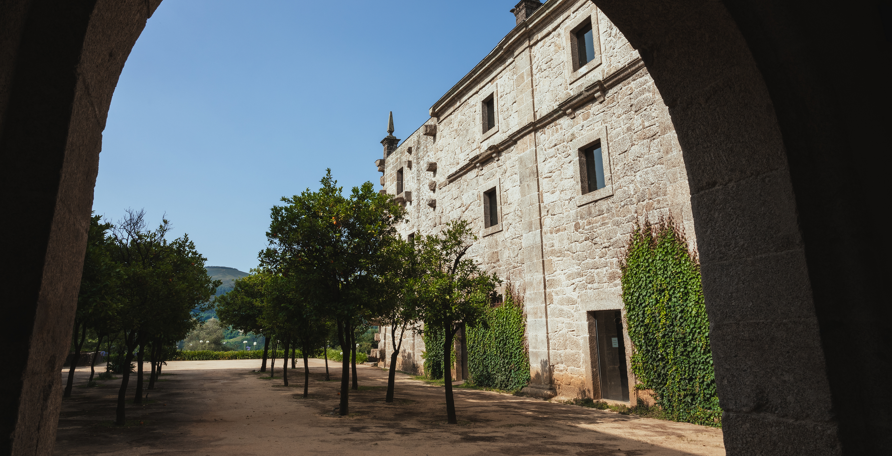Side facade of Pousada Mosteiro Amares, with a stone wall, trees, and a mountain in the background