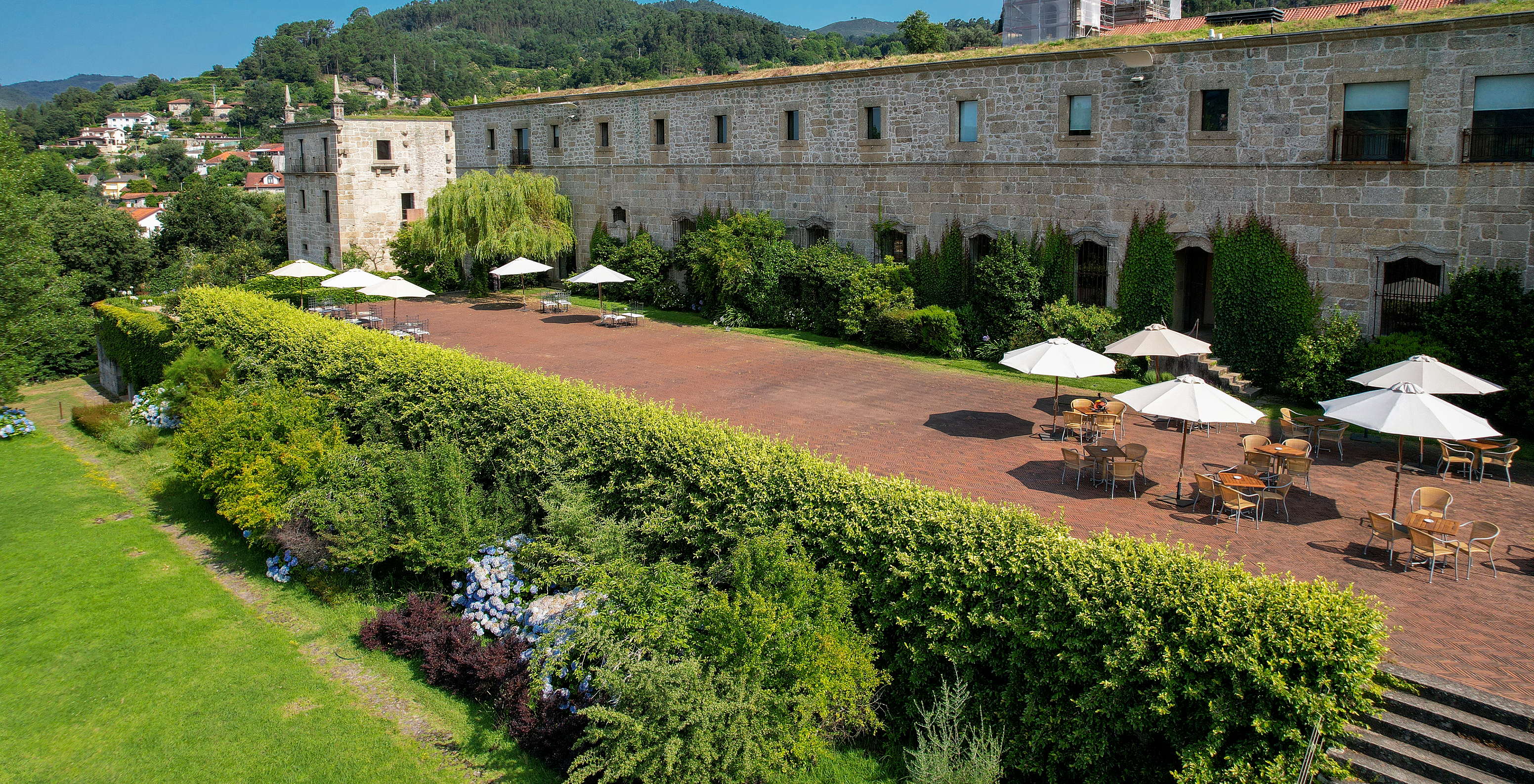 Aerial view of Pousada Mosteiro Amares’ exterior, with its stone building, terrace, grass, and greenery