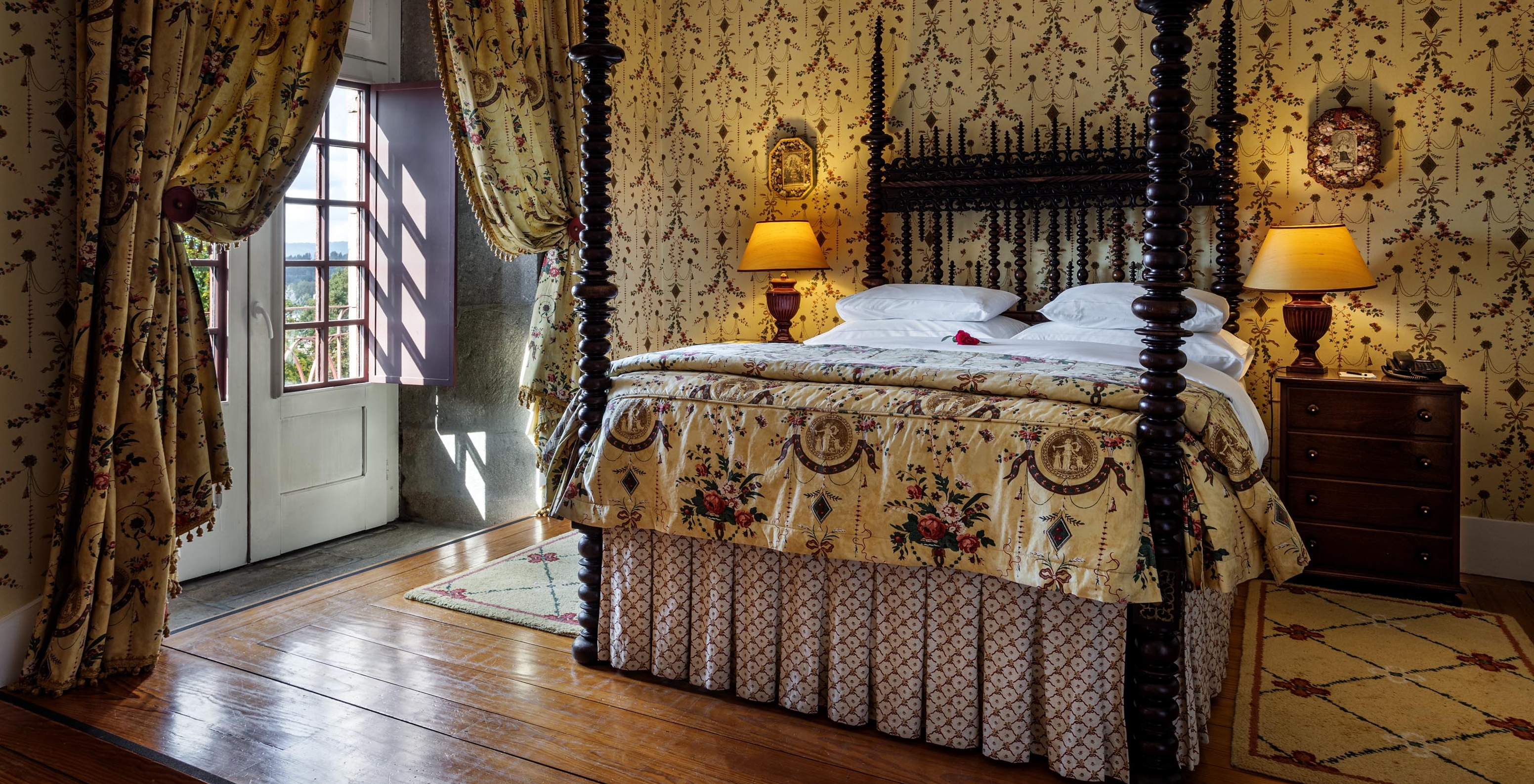 The Master Suite of The Pousada Mosteiro Guimarães has a dark wood double bed and wallpaper with a pattern