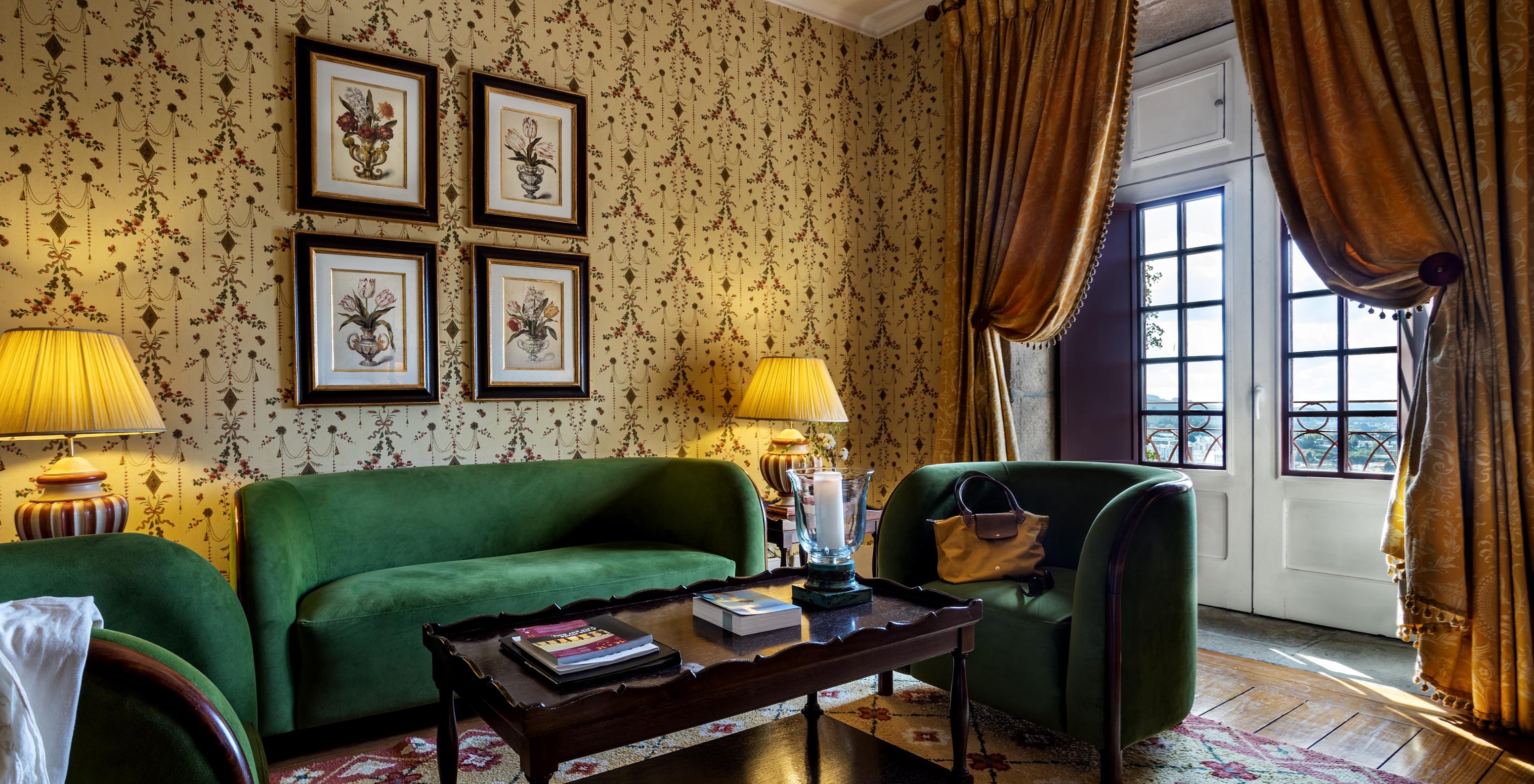 The Master Suite of The Pousada Mosteiro Guimarães features a sitting area with green sofas, a tall window, and paintings