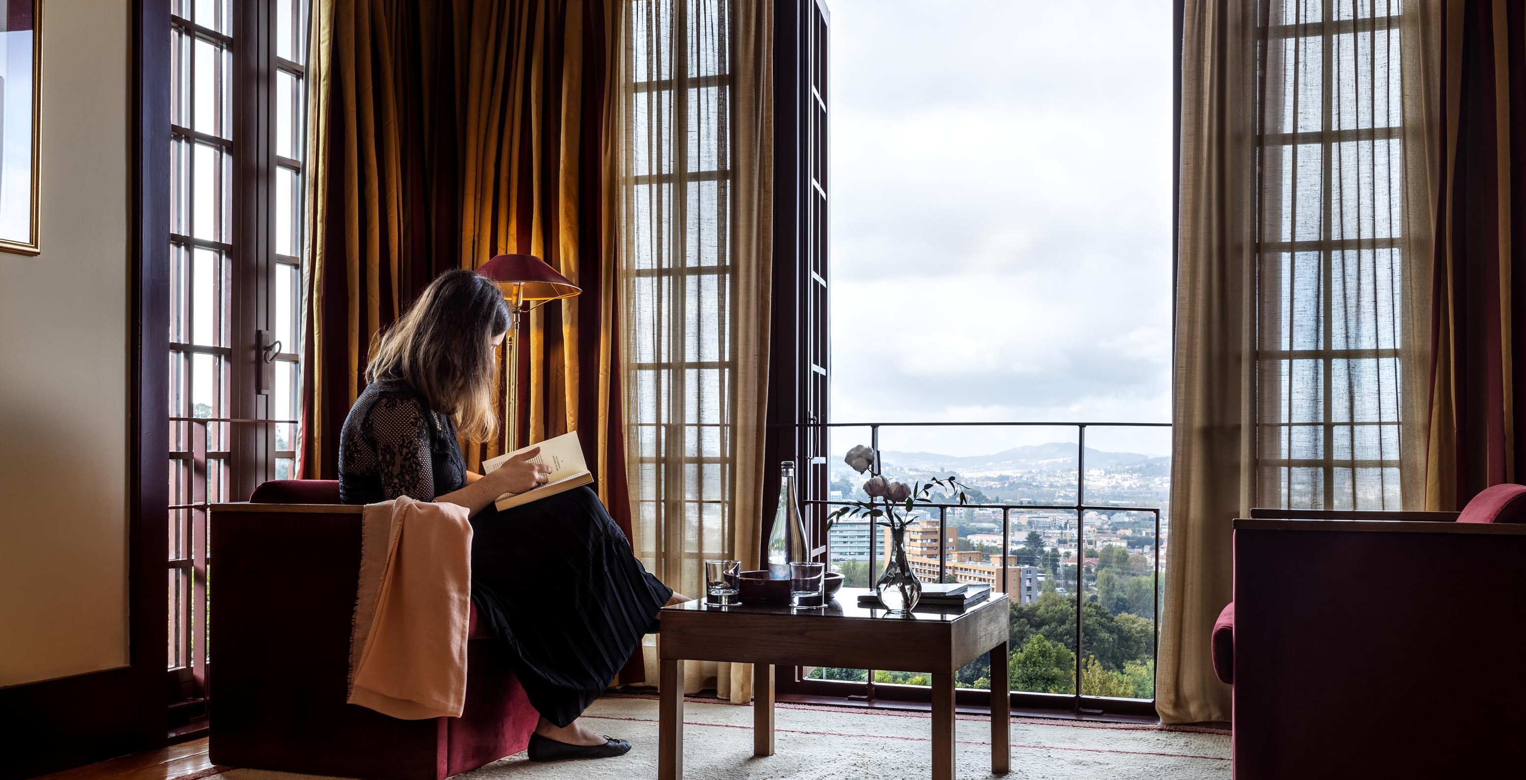 The Superior Room of The Pousada Mosteiro Guimarães has a sofa and a large window with a view of the city