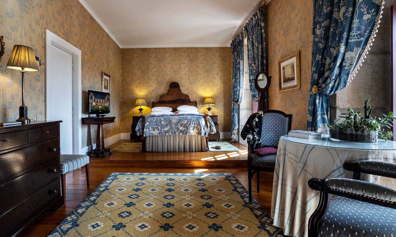 The Master Suite at Pousada Mosteiro Guimarães features blue tones, a double bed, table, chairs, and a dresser.