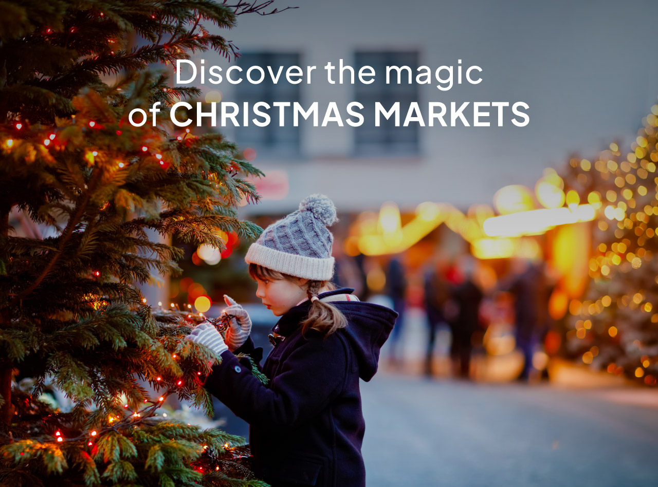 Child in winter hat decorating a lit Christmas tree at a festive market with glowing holiday lights