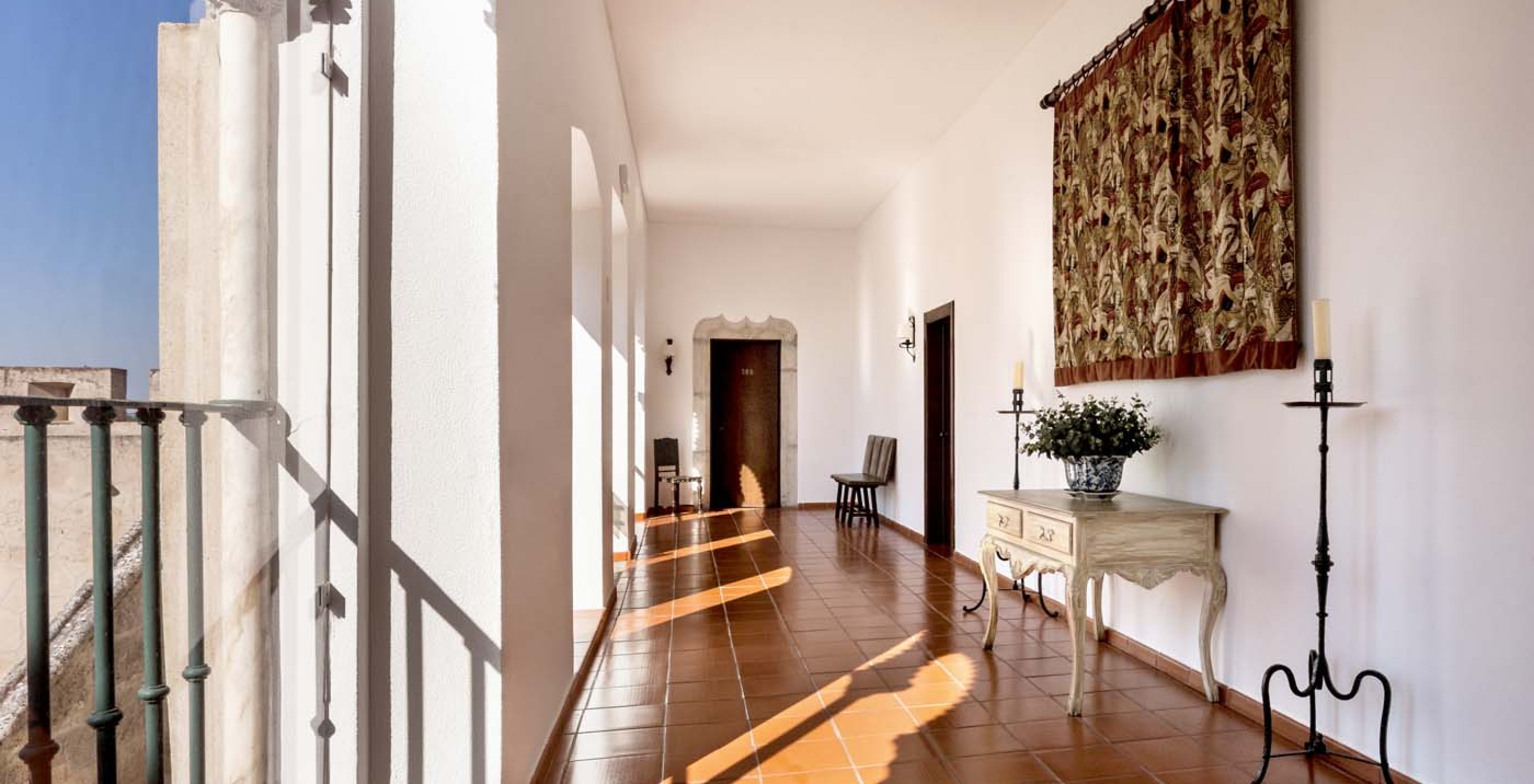 Pasillo de habitaciones con pequeño mueble y tapices en la Pousada Castelo Alvito, Hotel en Alvito