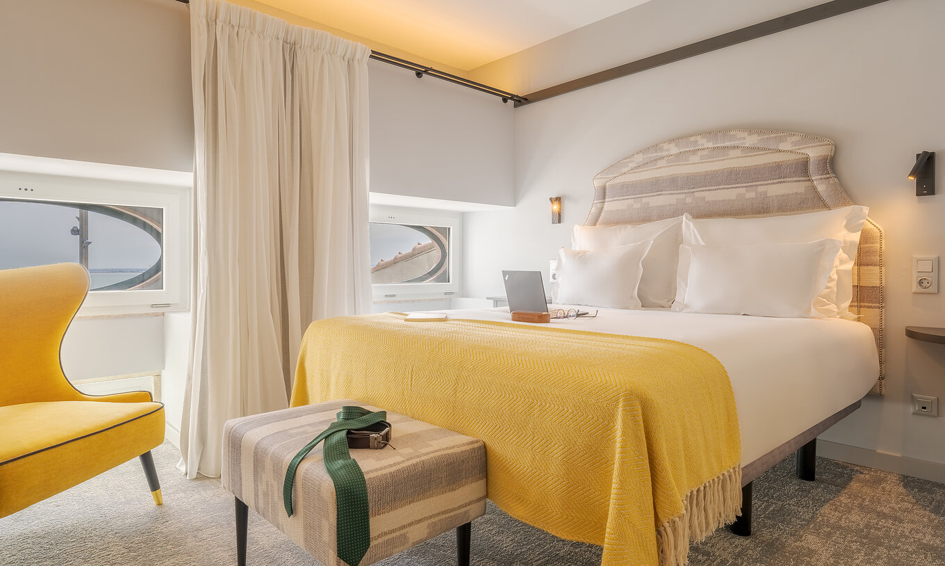 El Superior River View de la Pousada Alfama tiene una cama doble con una manta amarilla, vistas al río y un sillón amarillo