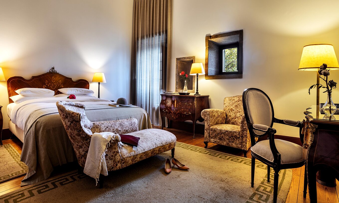 La Suite Histórica de la Pousada Mosteiro Guimarães tiene una cama matrimonial con un chaise longue al pie y un sillón