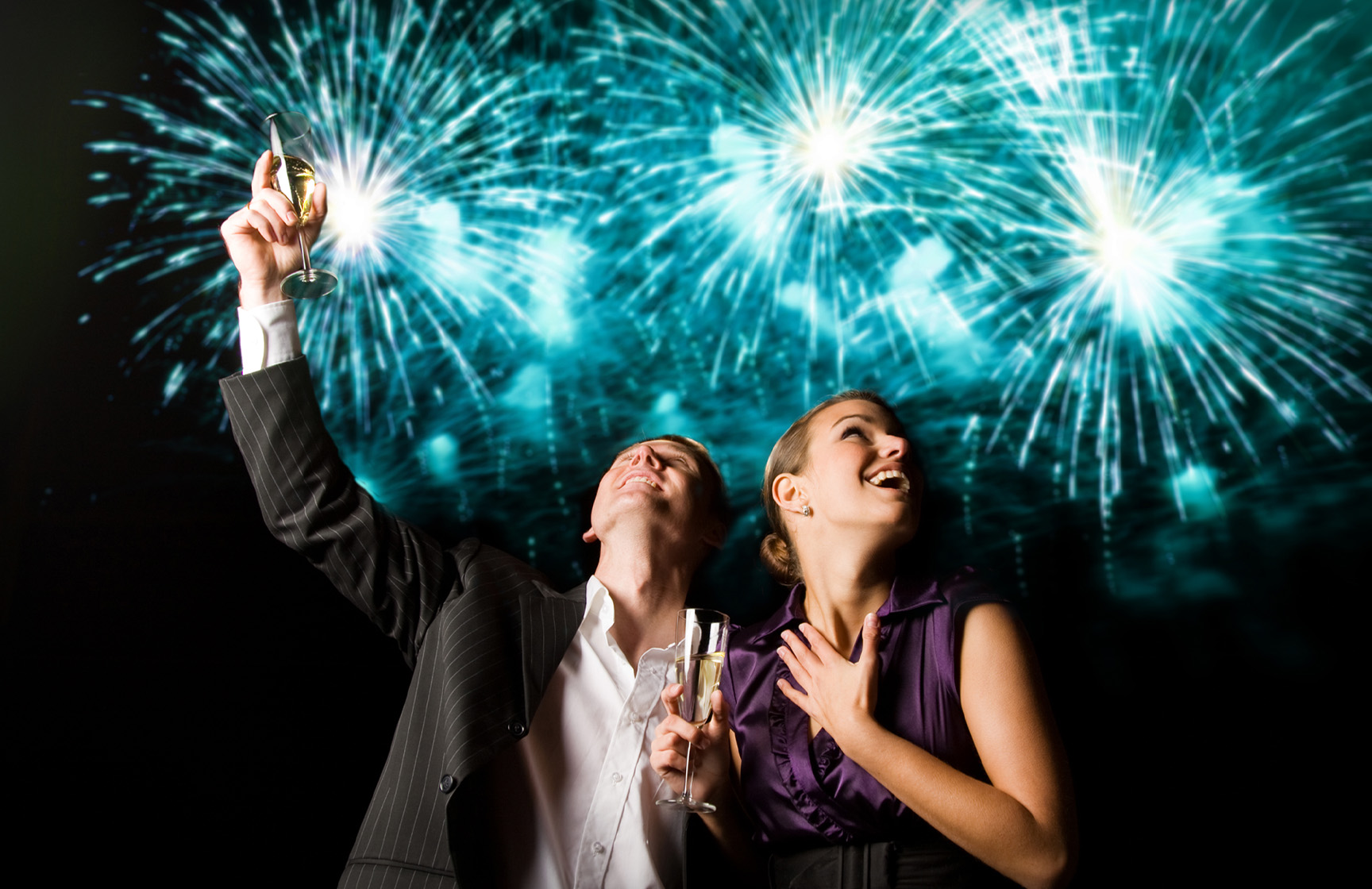 Pareja celebrando el Año Nuevo, con fuegos artificiales azules detrás, en una fiesta en un hotel del Pestana Hotel Group