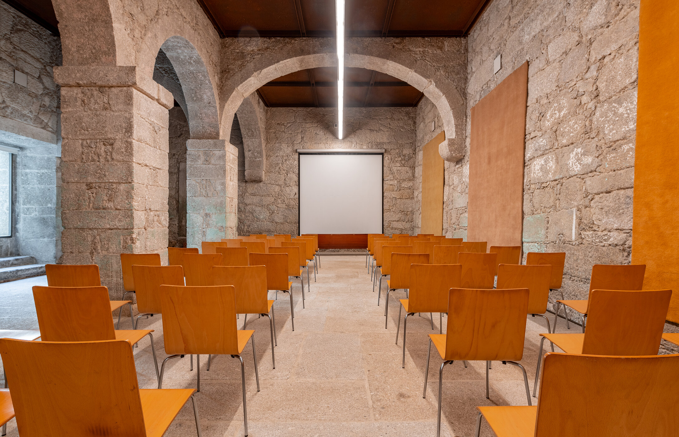 Auditorio amplio con varias sillas para reuniones o conferencias, en una sala histórica con paredes de arcos de piedra