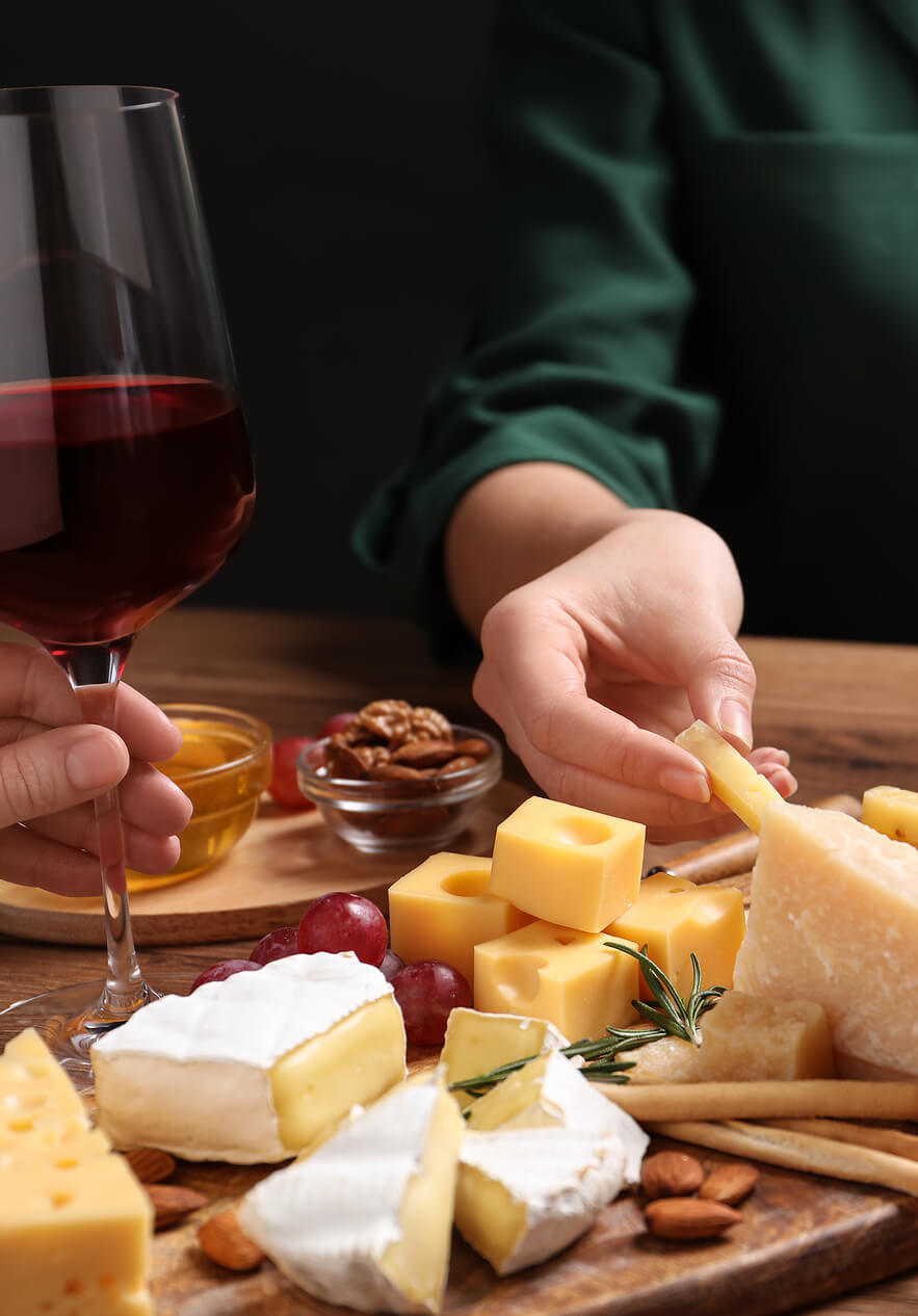 Tabla con quesos variados, uvas y frutos secos junto a una copa de vino tinto durante una degustación