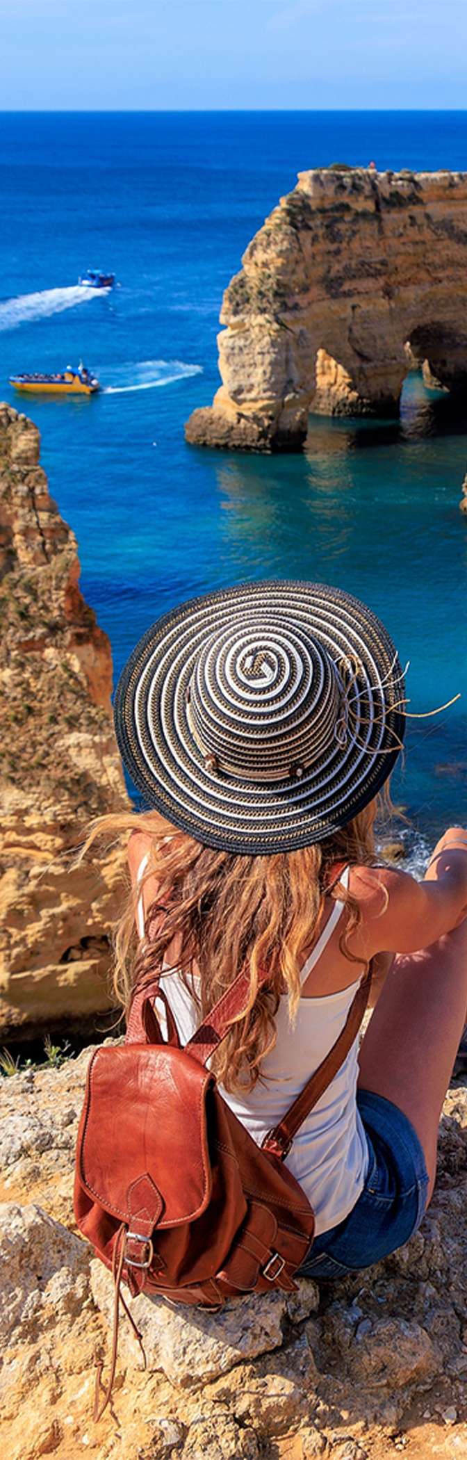 Mujer admirando la vista panorámica de la costa del Algarve, con aguas cristalinas y un acantilado rodeado de vegetación
